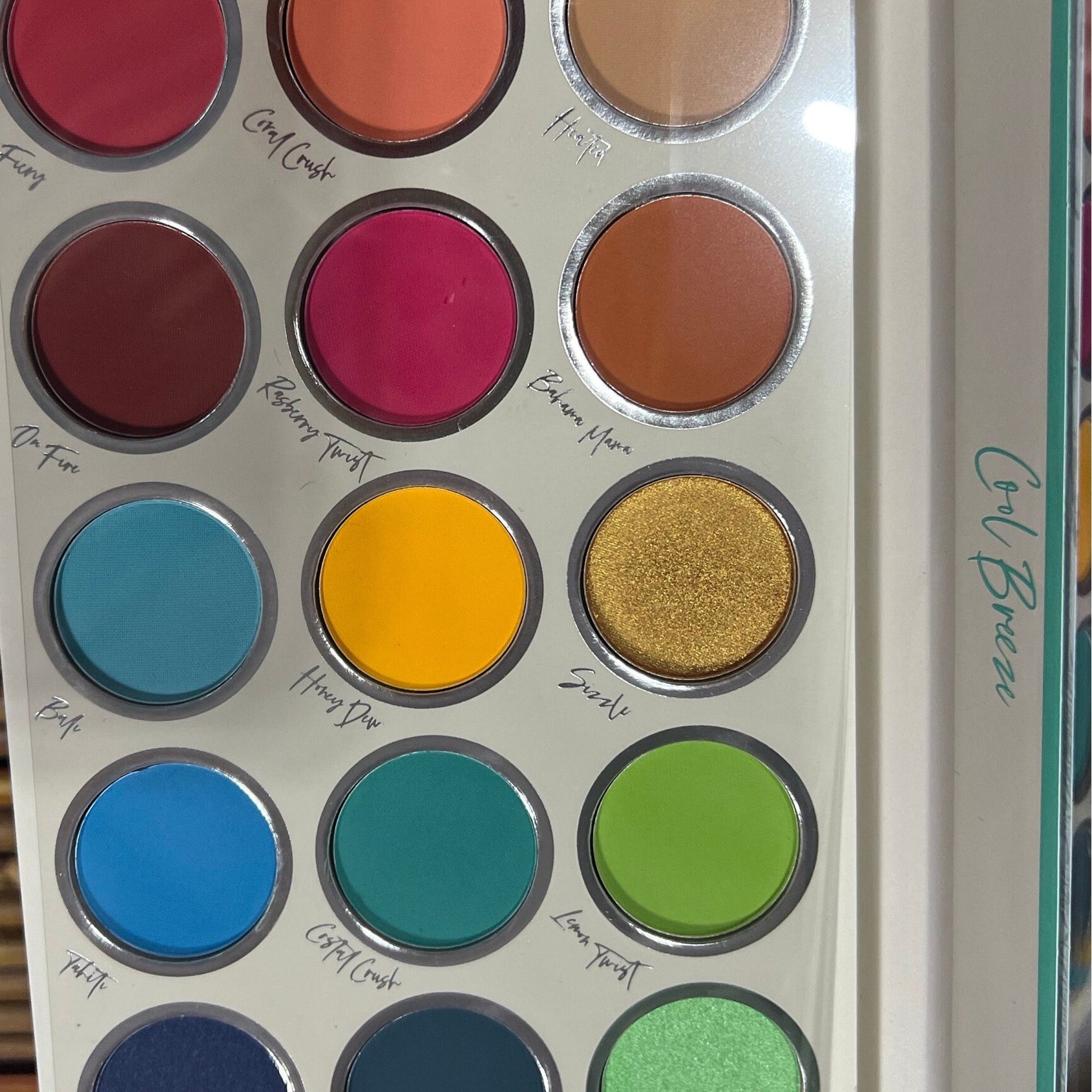 Eyeshadow palette with multiple colors, including pink, blue, and gold, in a round compact, "Cool Breeze" text visible