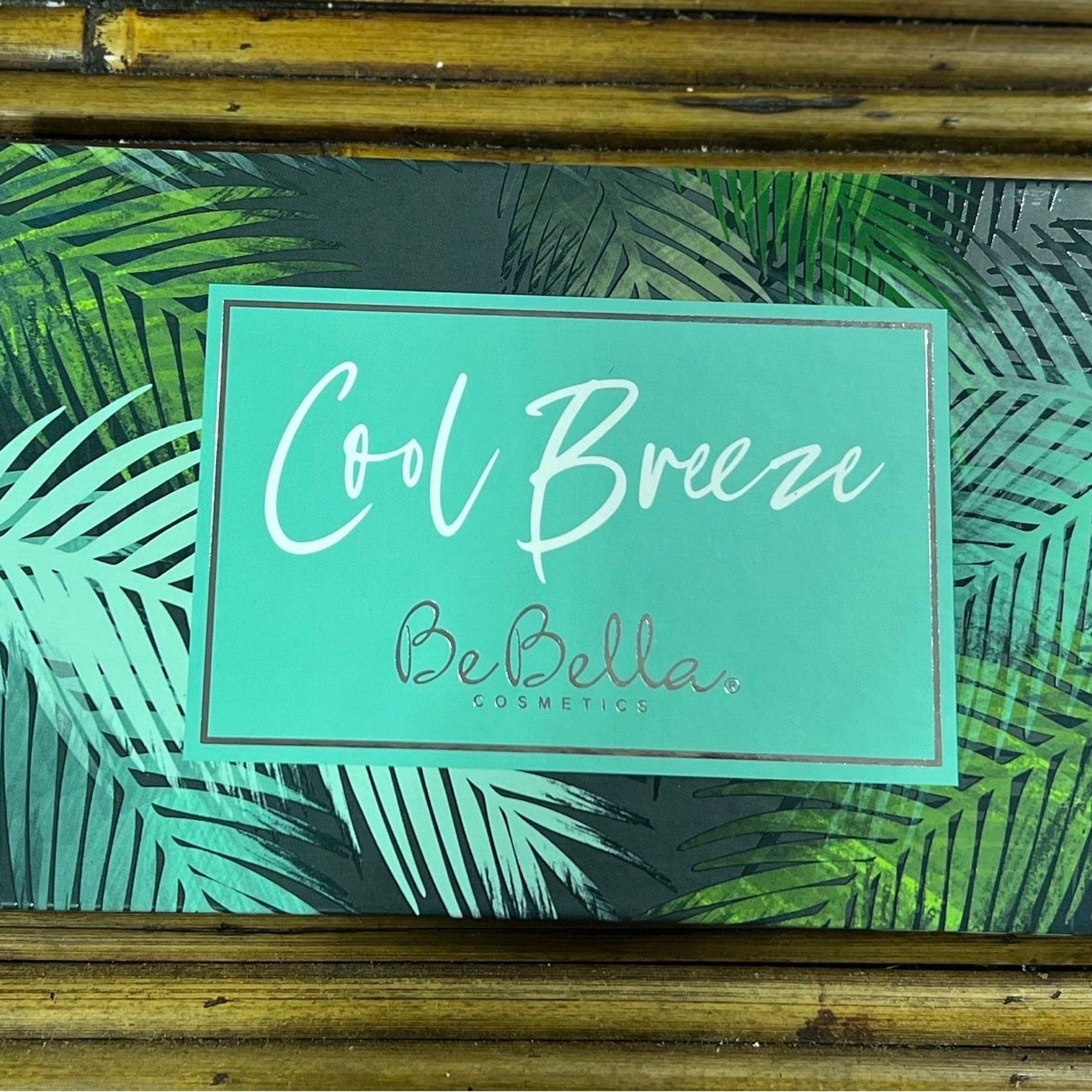 Cosmetics palette with teal and silver accents, "Cool Breeze" text, and BeBella brand name on a palm leaf pattern background.