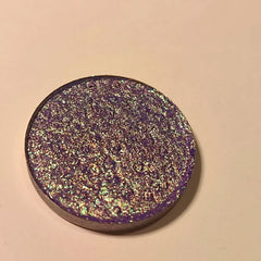 Close-up of a makeup brush applying vibrant blue-violet eye shadow to eyelid, showcasing rich pigment and smooth blendability