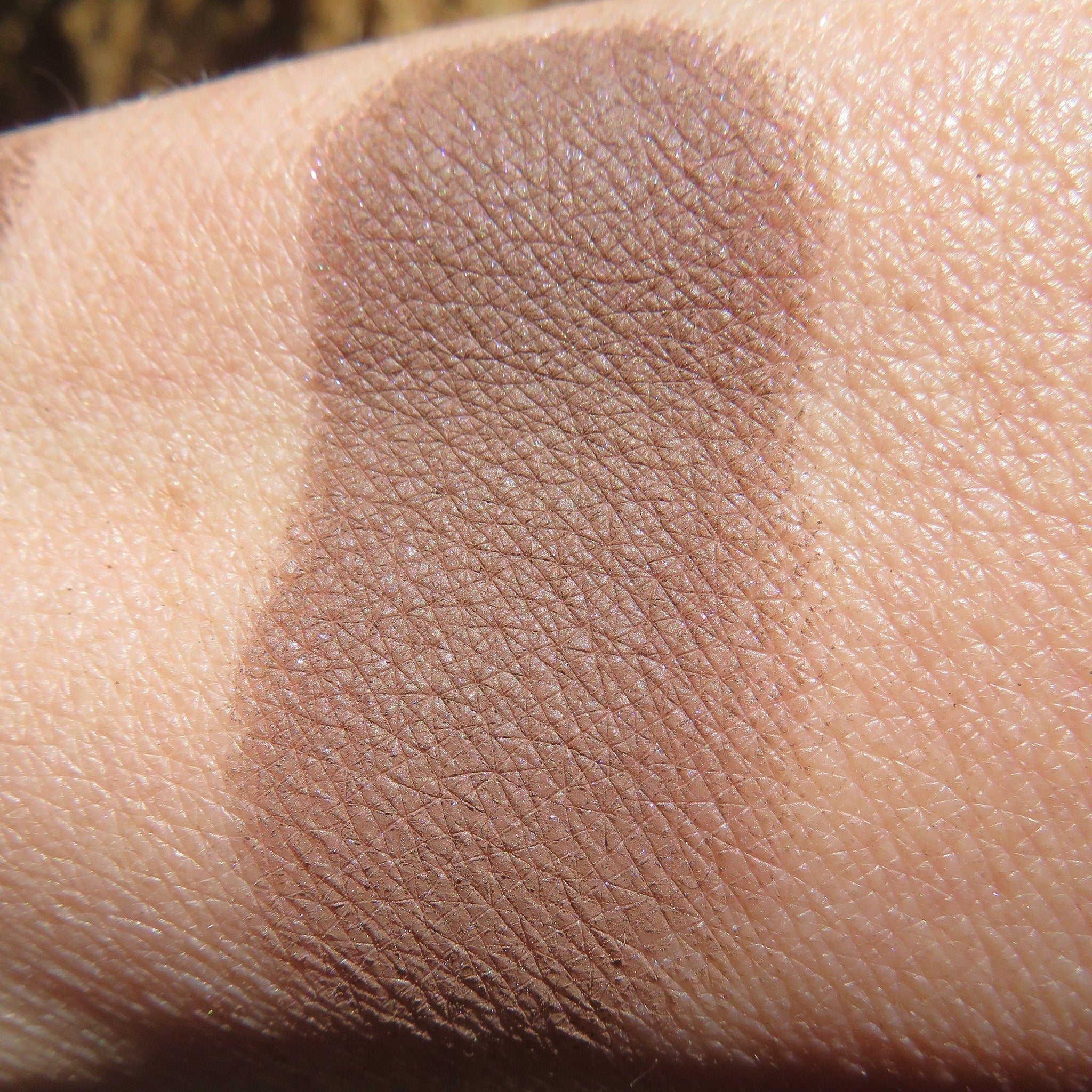 Brown eyeshadow swatch on skin, showing color, texture, and application on the arm