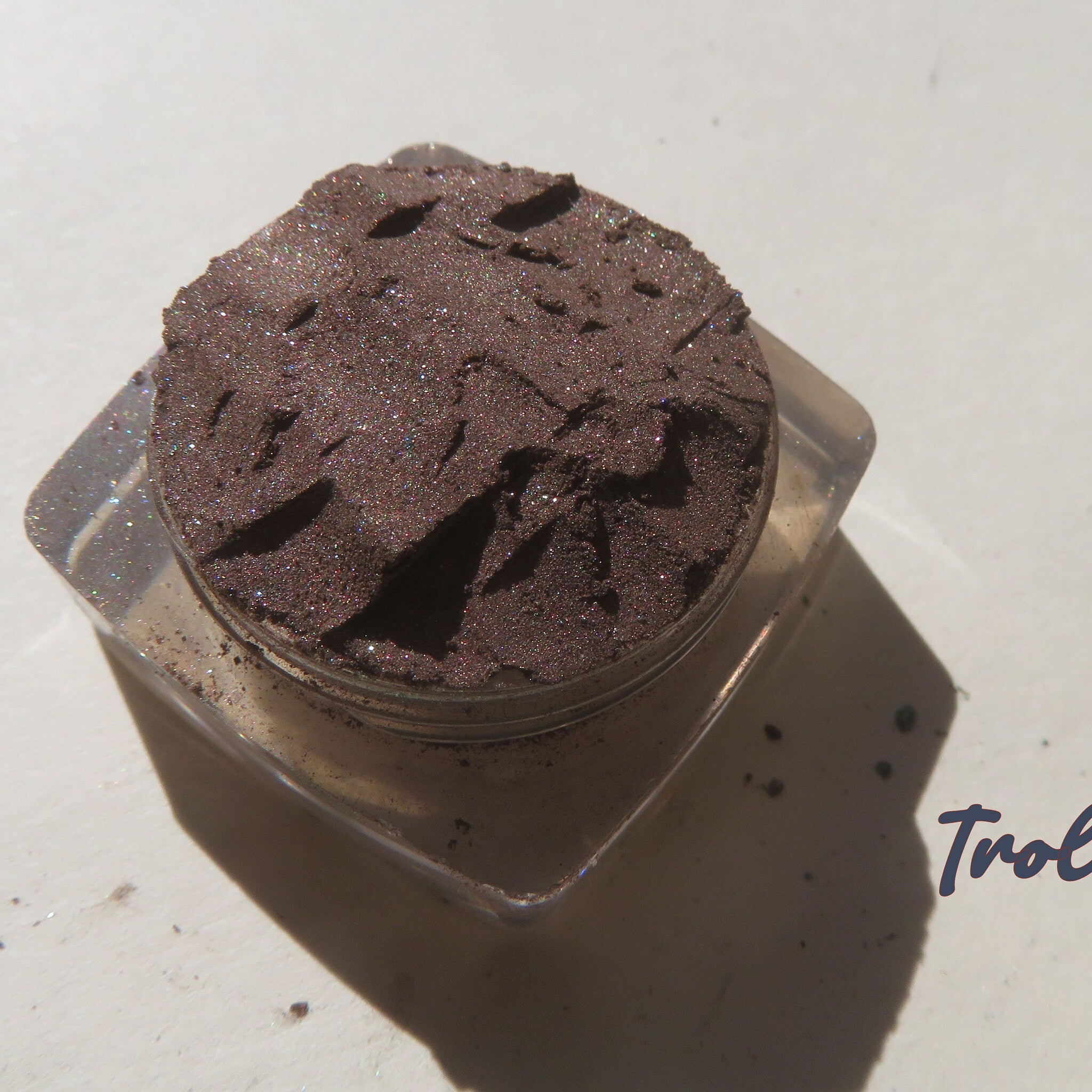 Side angle view of loose mineral eyeshadow in rich dark brown shimmer pigment, showcasing fine sparkle texture
