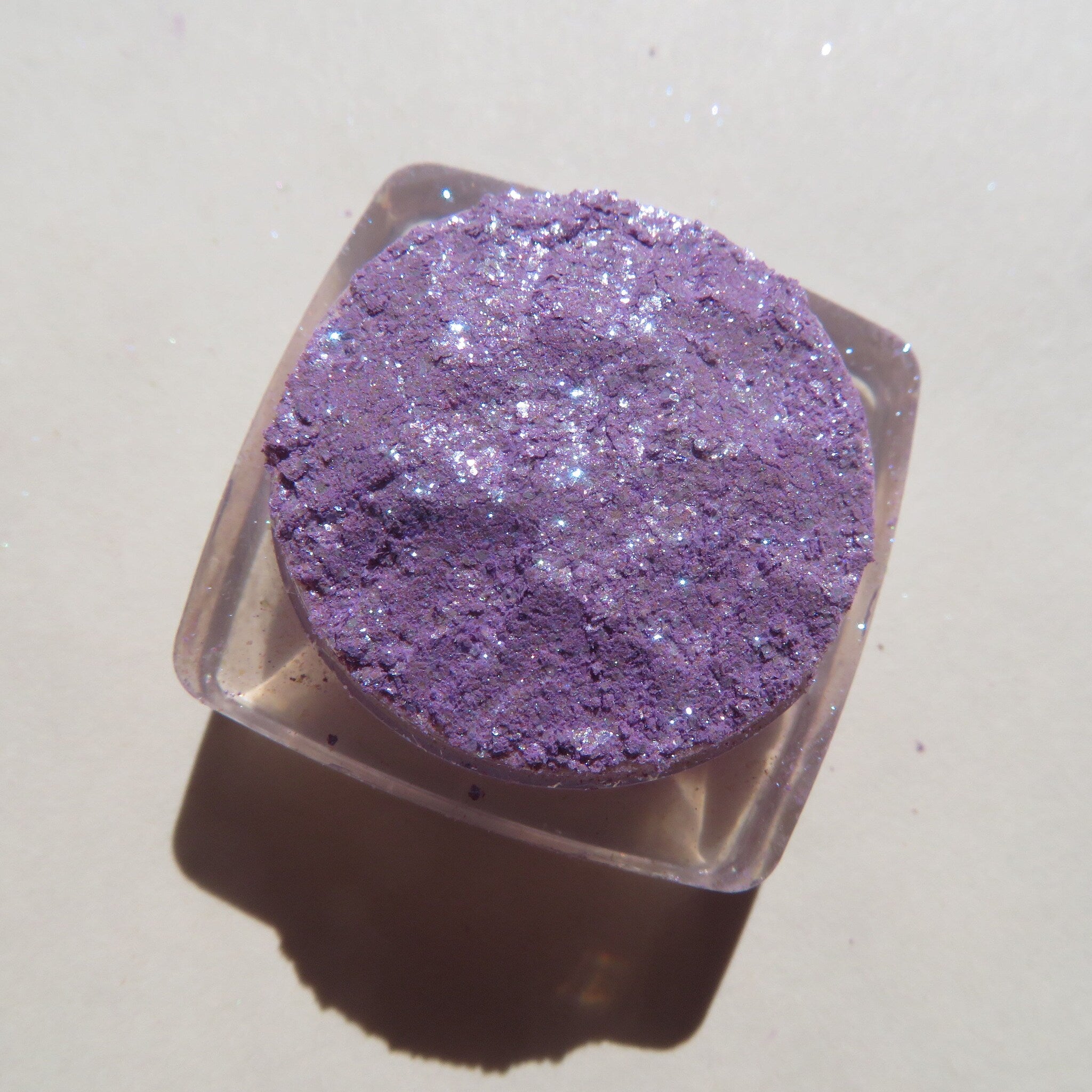 Close-up of fingers applying sparkly violet and blue glitter eyeshadow to eyelid with shimmer effect