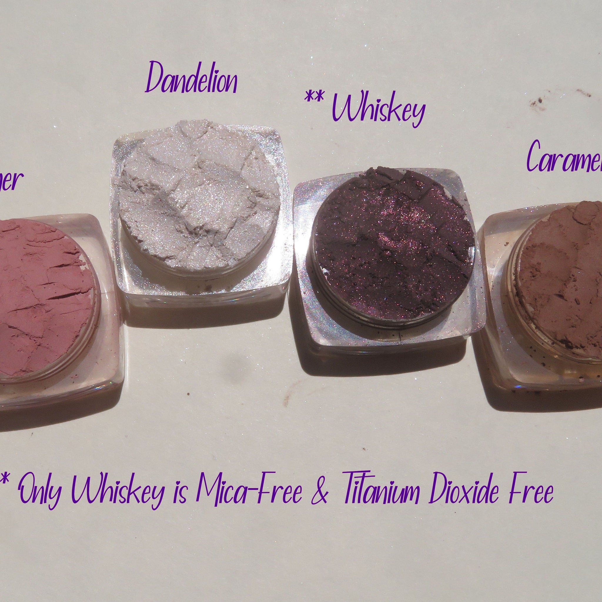 Side view of four loose mineral eyeshadows in matte peach, shimmer bronze, matte mauve, and metallic gold with sifter jars