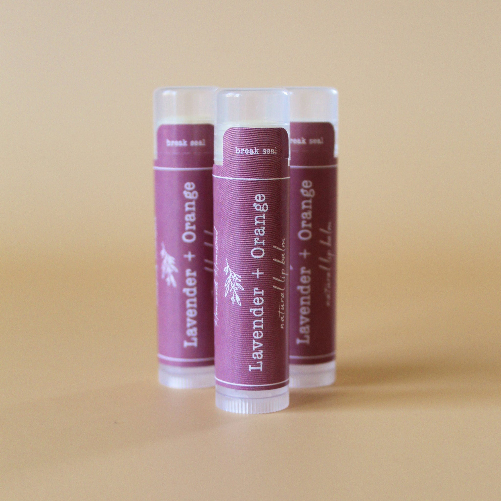 Lip balm tubes with purple label, white text, and clear plastic cap, Lavender + Orange flavor