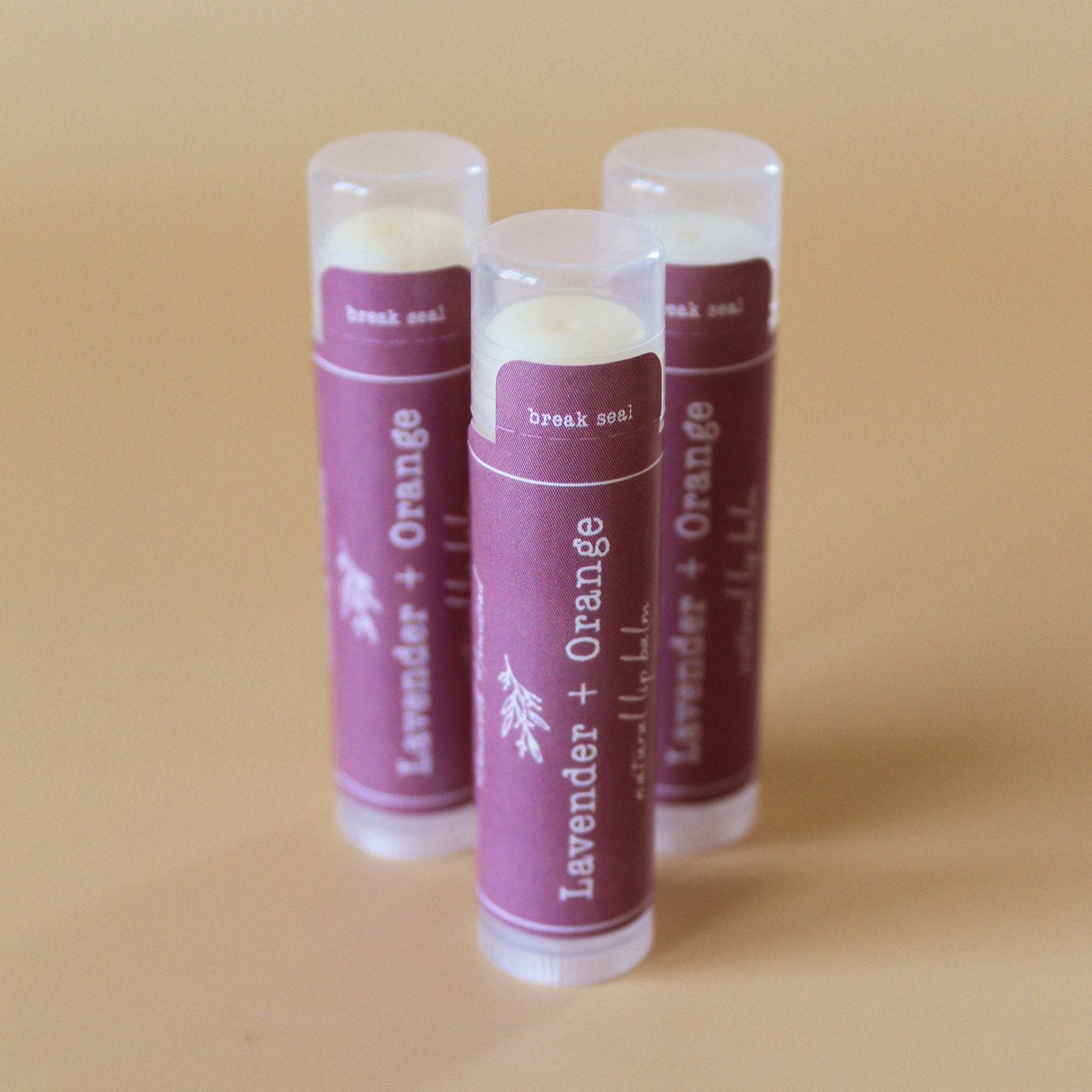 Lip balm tubes with purple label, clear cap, and white text, "Lavender + Orange