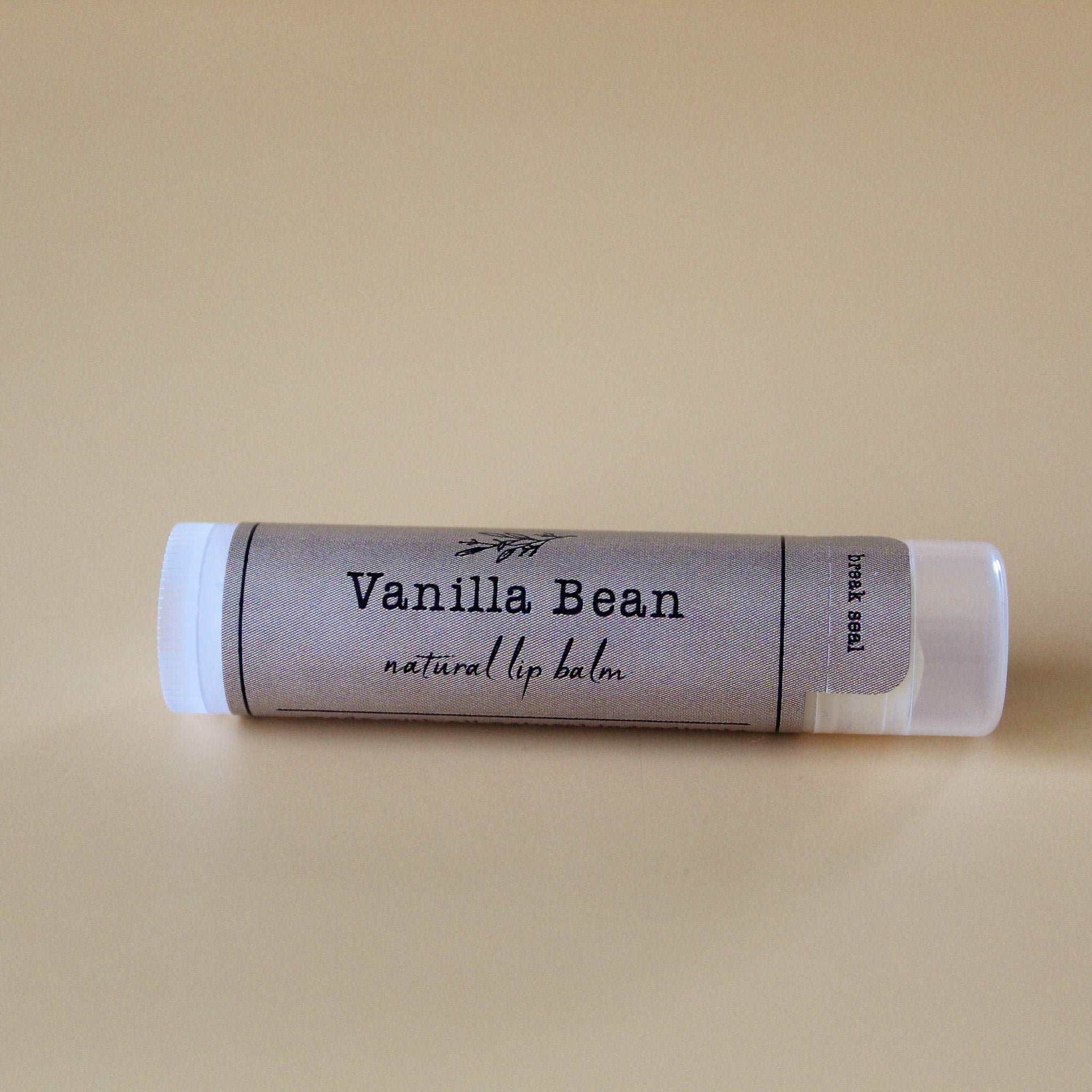 Lip balm tube with gray patterned label, white cap, and "Vanilla Bean" text