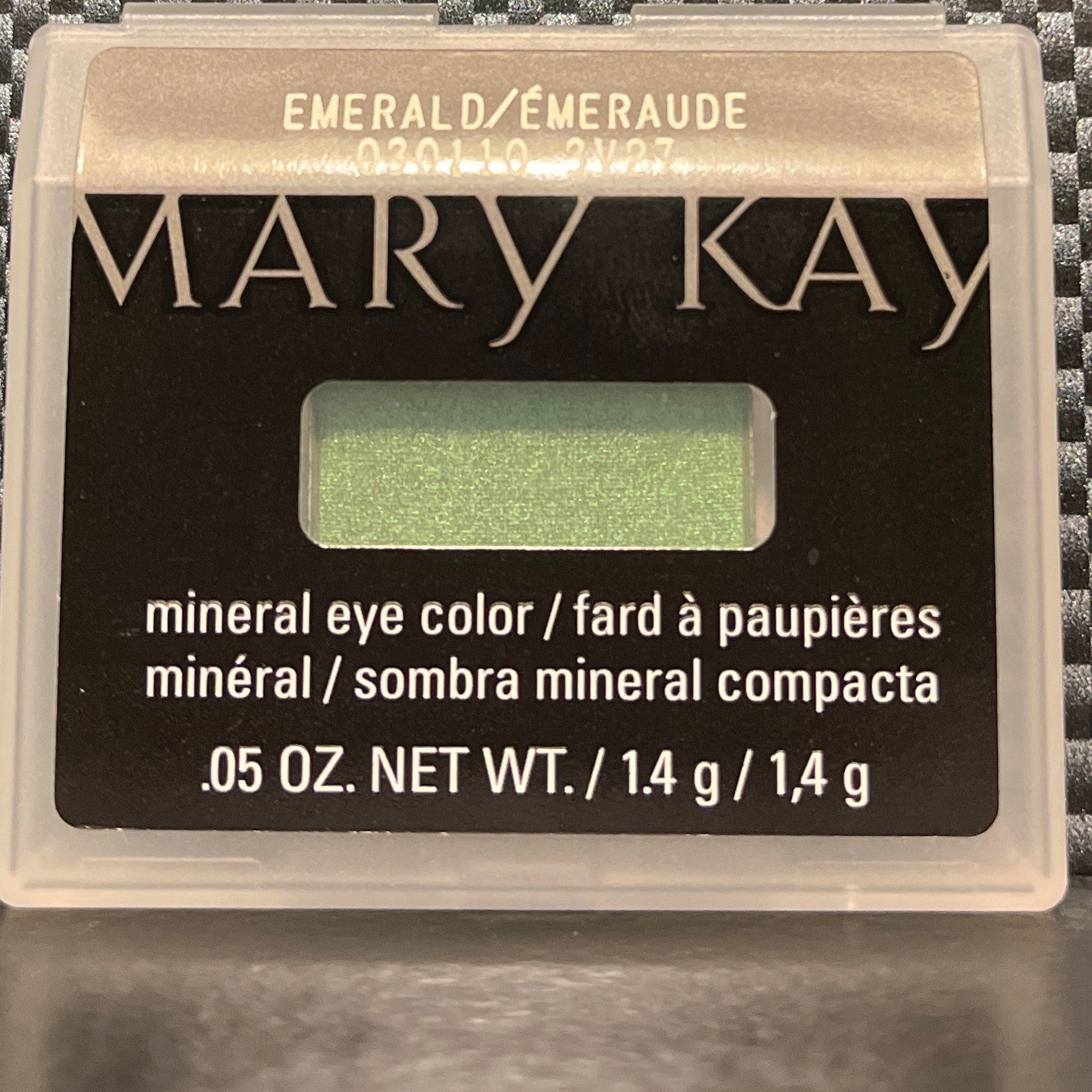 Side angle view of shimmering emerald mineral eye shadow in compact, showcasing reflective green sparkle and smooth texture