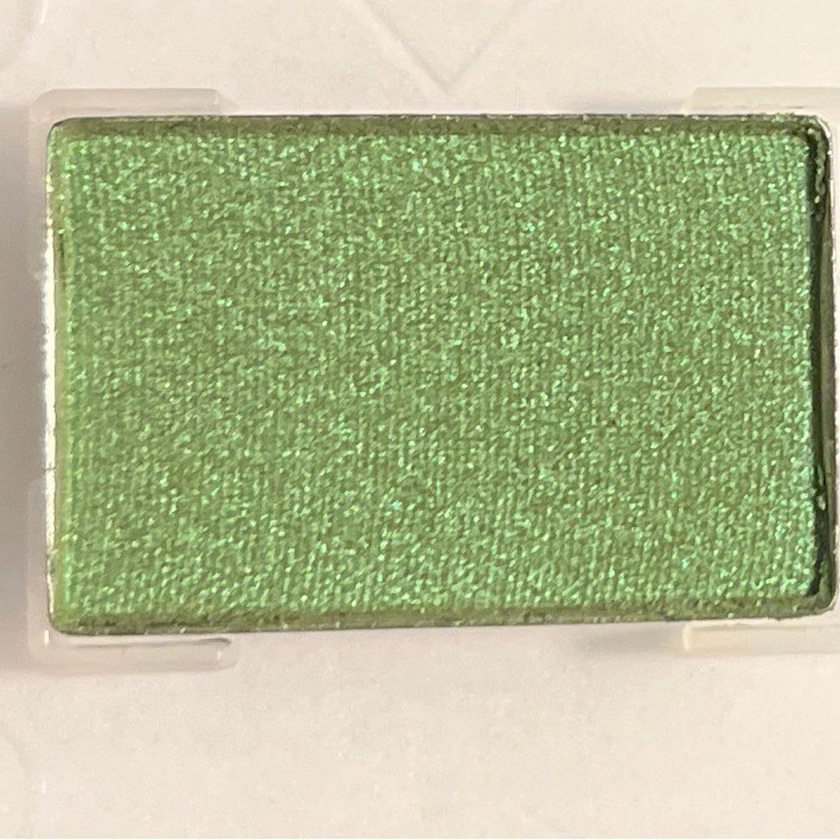 Shimmering emerald green mineral eye shadow in compact with reflective metallic casing and visible powder texture.