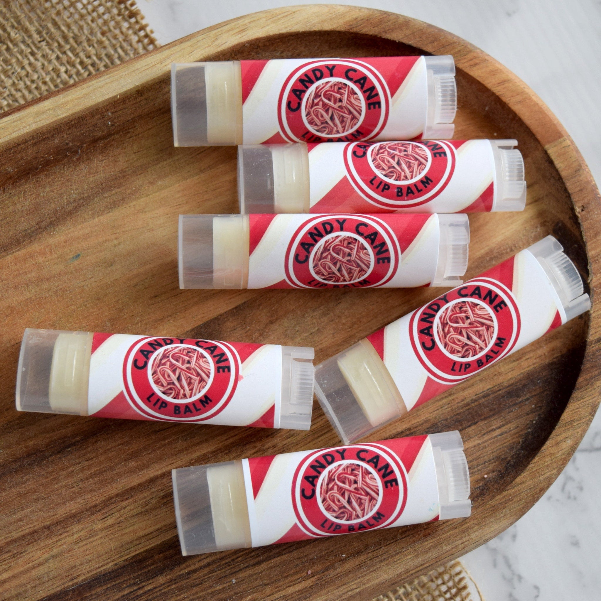 Candy Cane Lip Balm tubes with red and white label, clear plastic cap, arranged on wooden tray