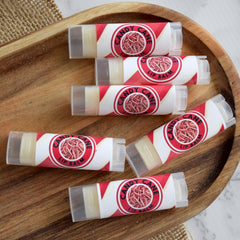 Candy Cane Lip Balm tubes with red and white label, clear plastic cap, arranged on wooden tray
