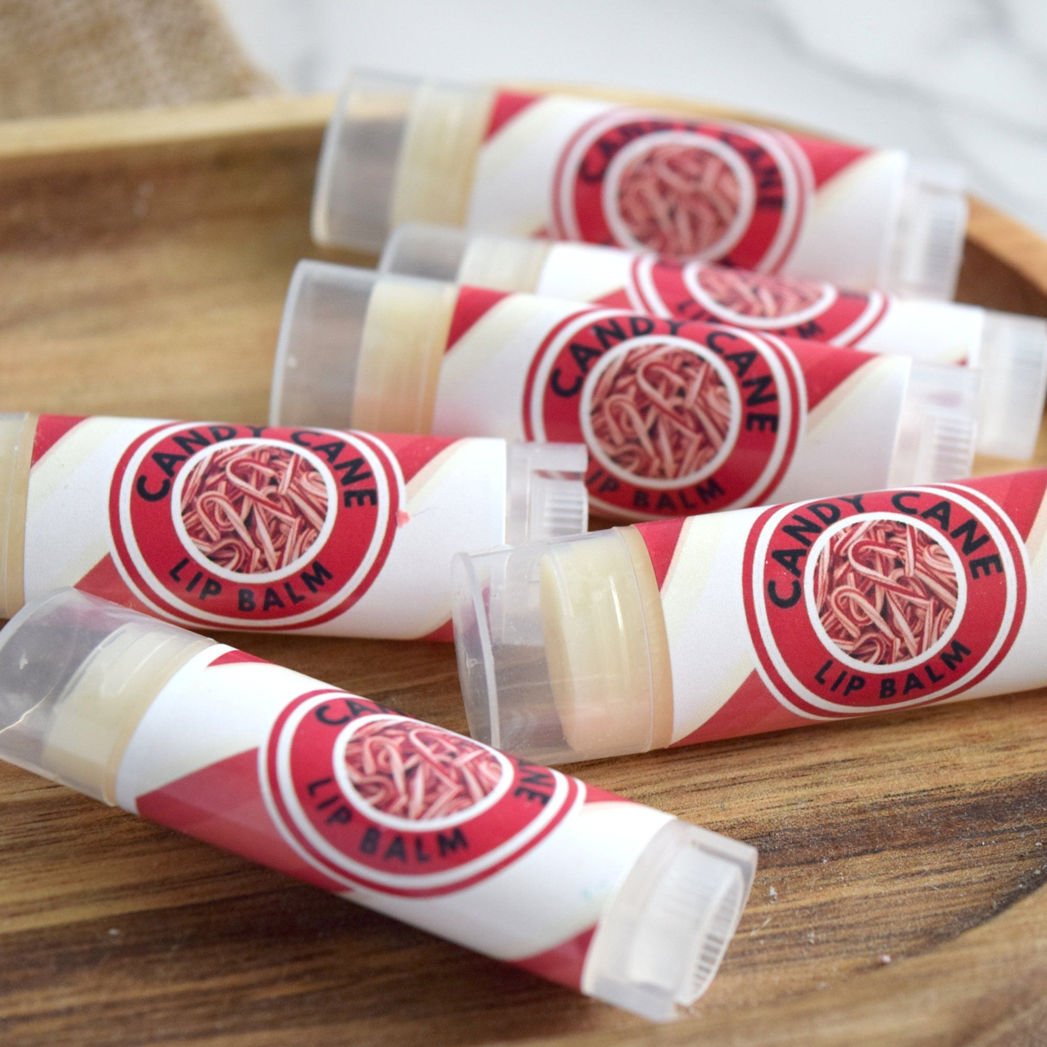 Lip balm tubes with red and white labels, candy cane pattern, and clear caps on a wooden tray