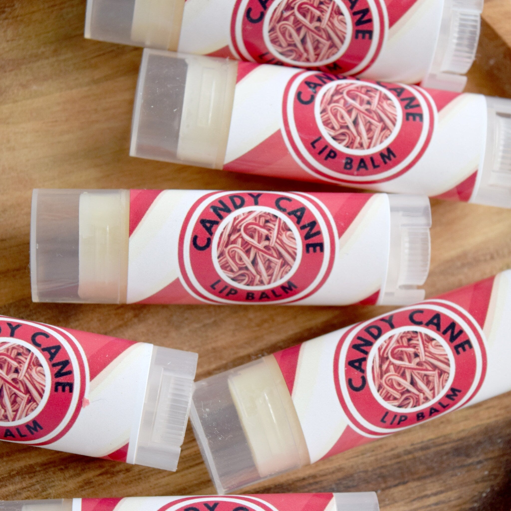 Candy Cane lip balm tubes with red and white striped design and clear plastic caps on wooden surface