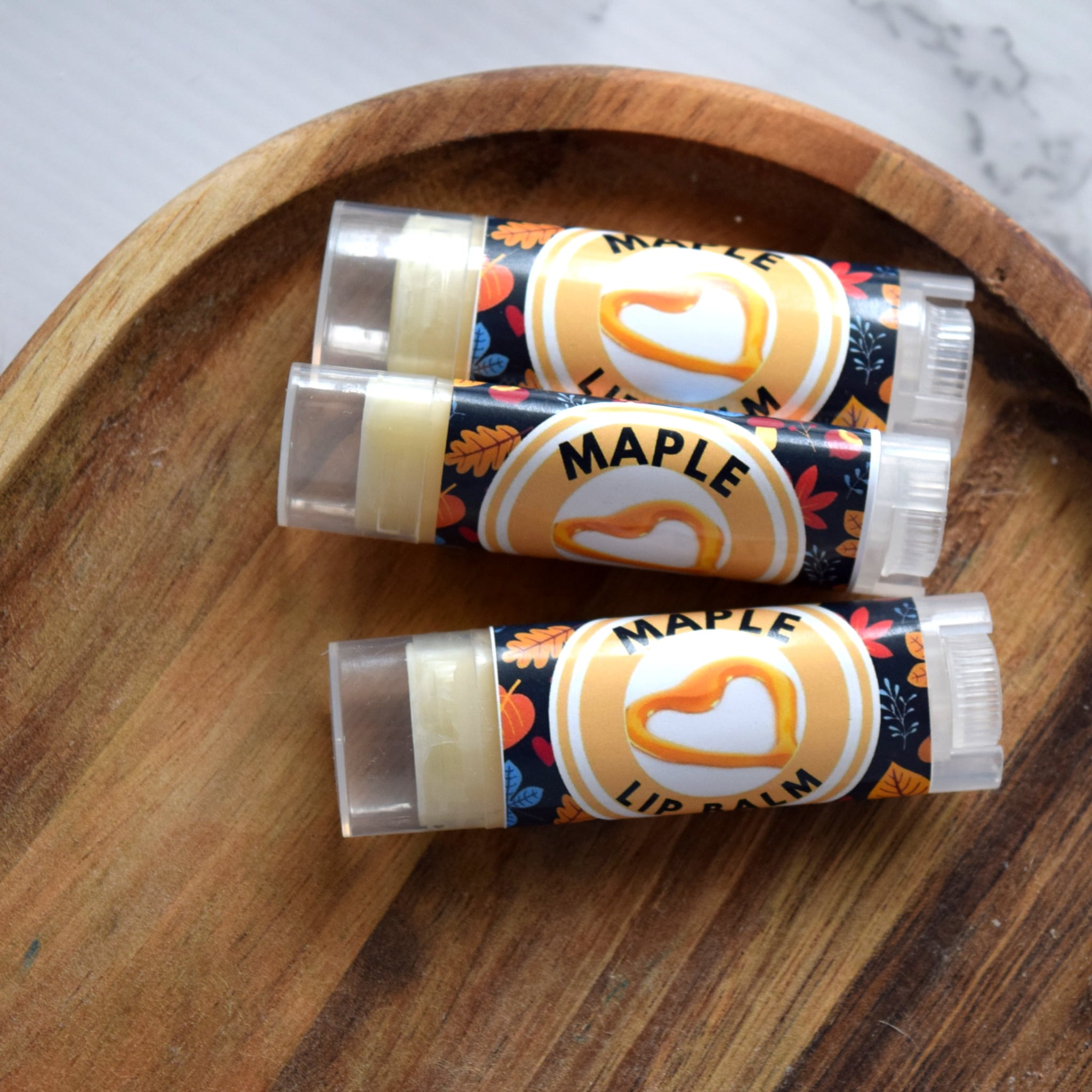 Lip balm tubes with maple label, clear tube, and wooden tray background