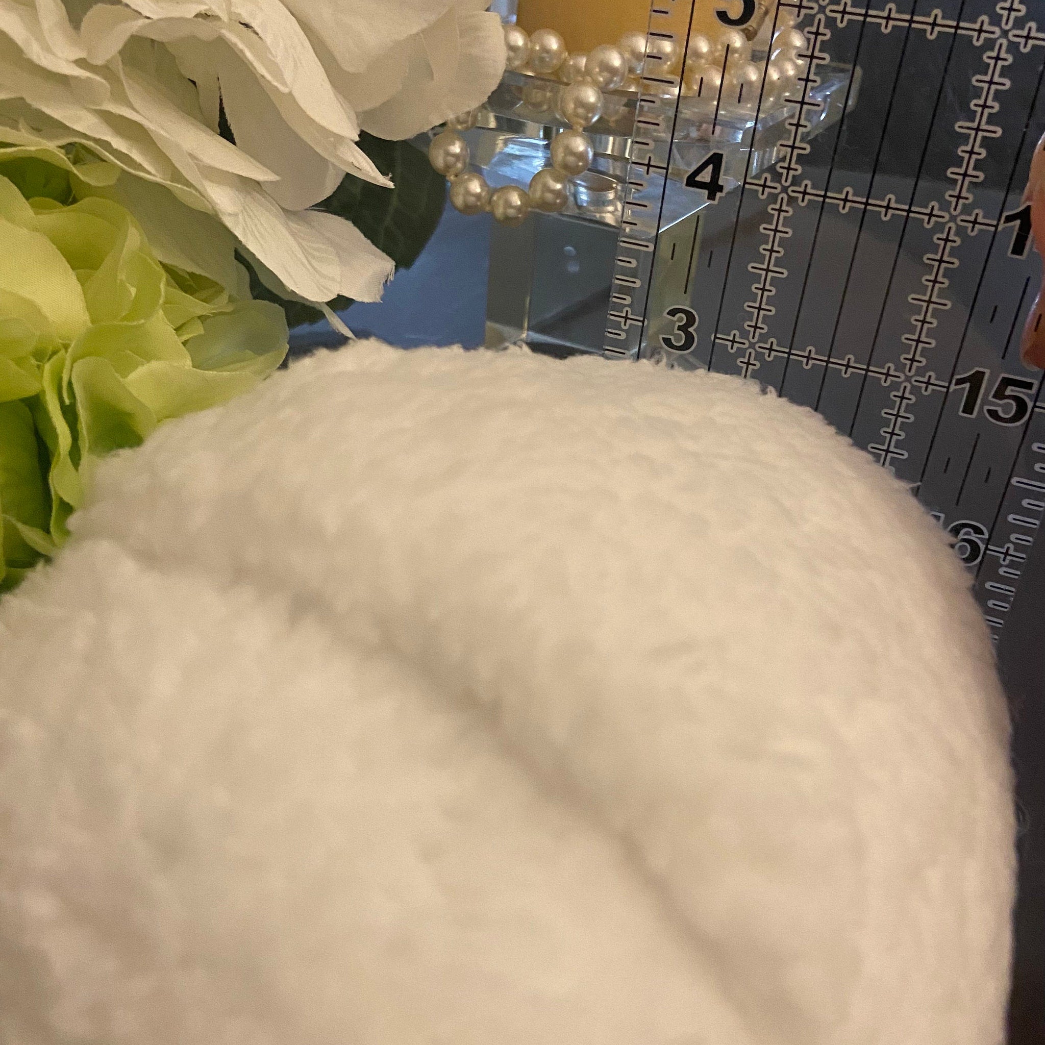 White plush material with light green and white floral accents next to a ruler