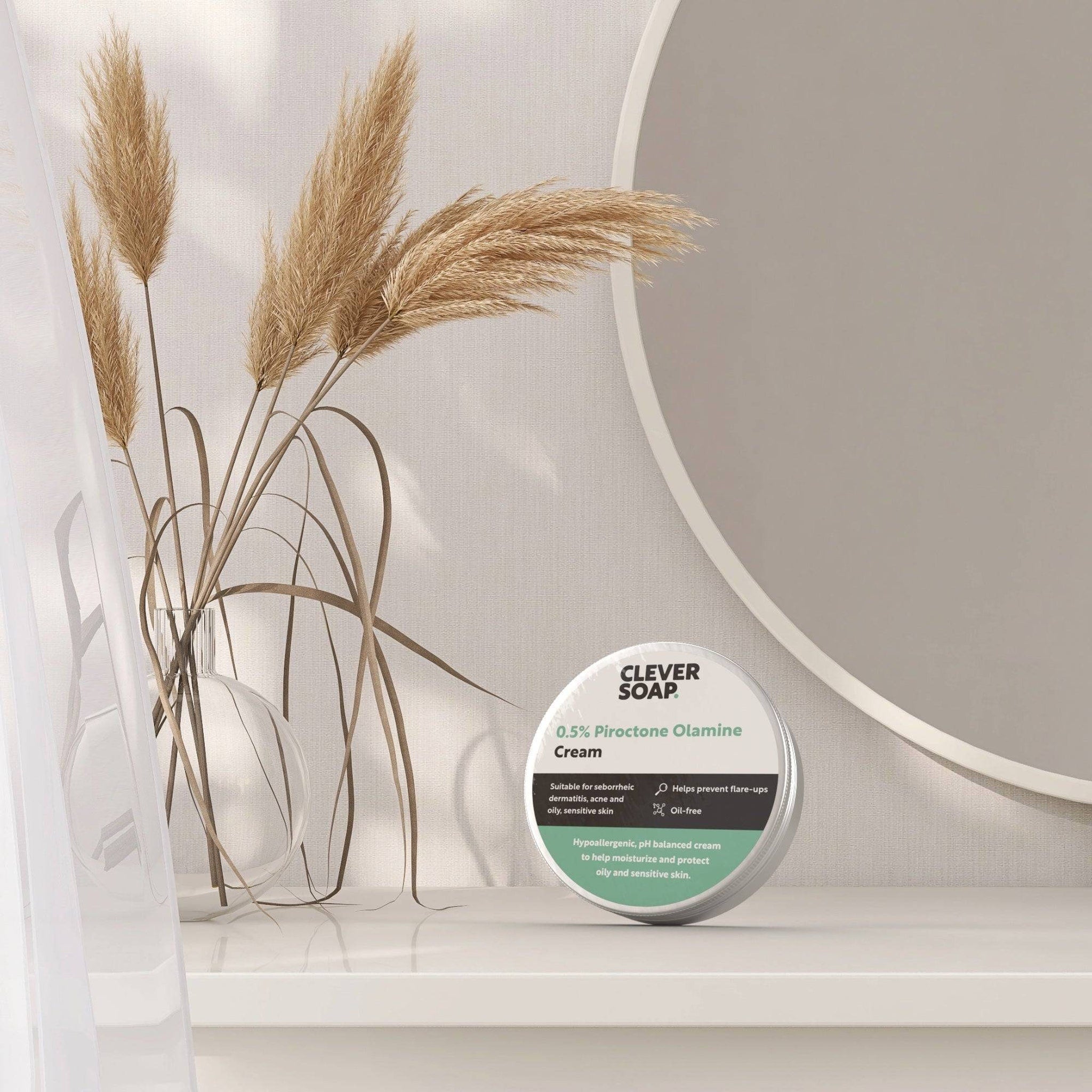 Cream jar with silver lid, white label, and text "CLEVER SOAP" on white surface near dried plants