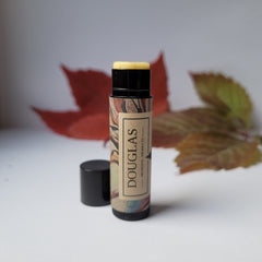 Lip balm tube with black cap, patterned label, and yellow balm visible, "DOUGLAS" printed