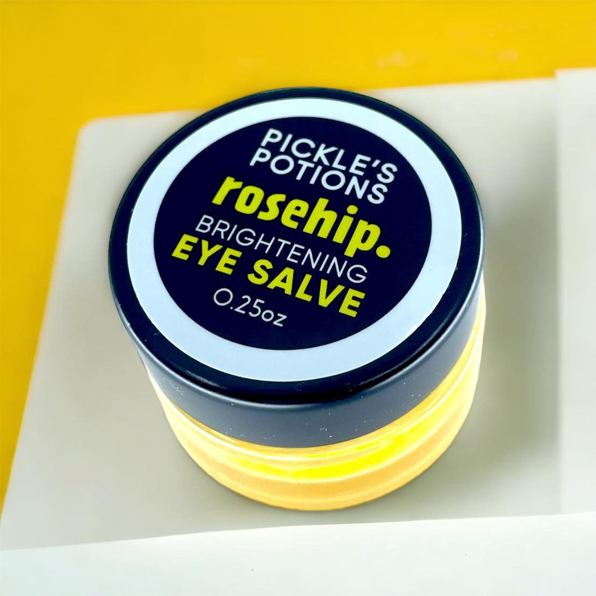 Eye salve jar with black lid, white text, and yellow contents, Pickle's Potions brand