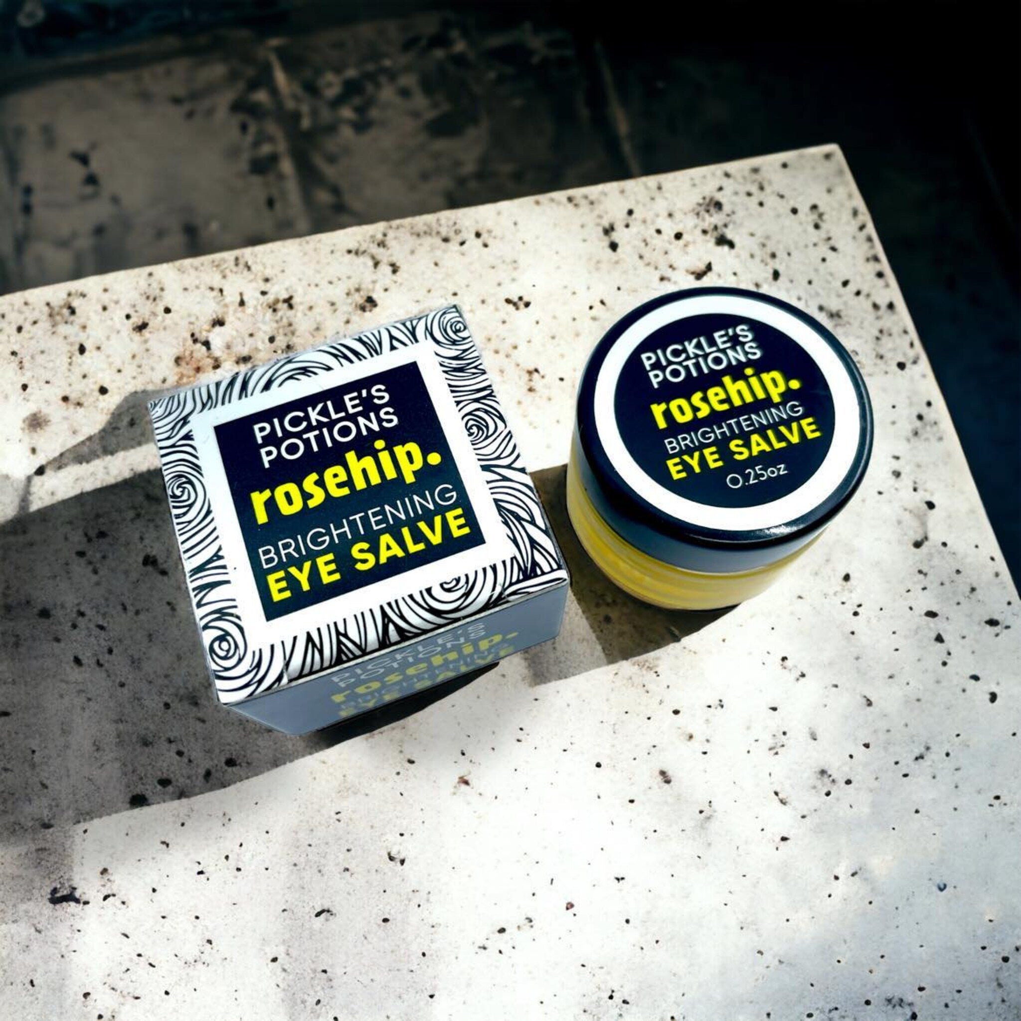 Eye salve with black lid and box, yellow cream, and white and black patterned box with text "Pickle's Potions" and "rosehip