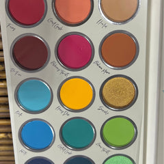 Eyeshadow palette with multiple colors including red, pink, yellow, and green in circular pans, silver rims, and text labels.