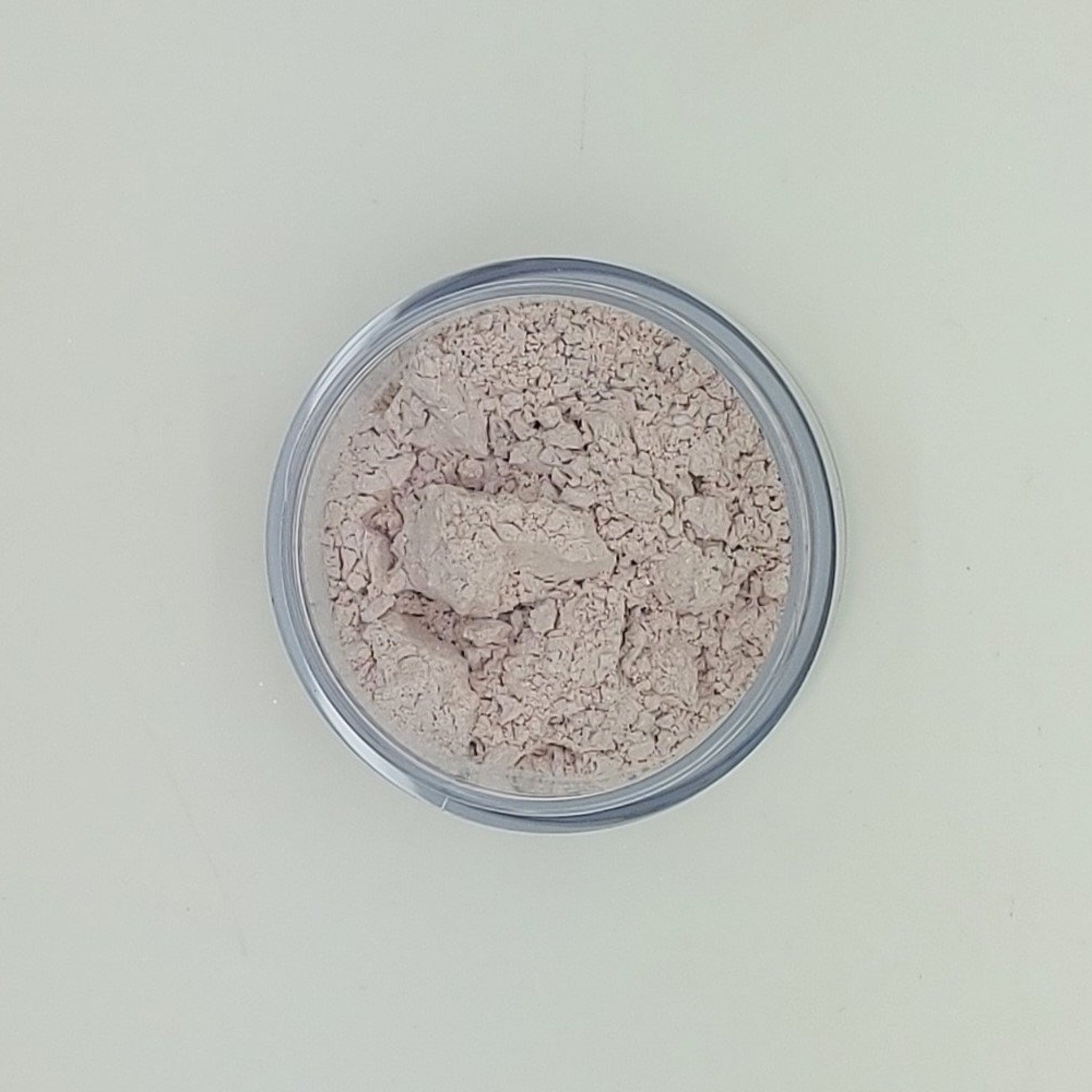 Powder makeup in a clear plastic container, light beige color, granular texture