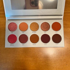 Eyeshadow palette with ten round shades in various colors, including red, orange, and brown, with a mirror
