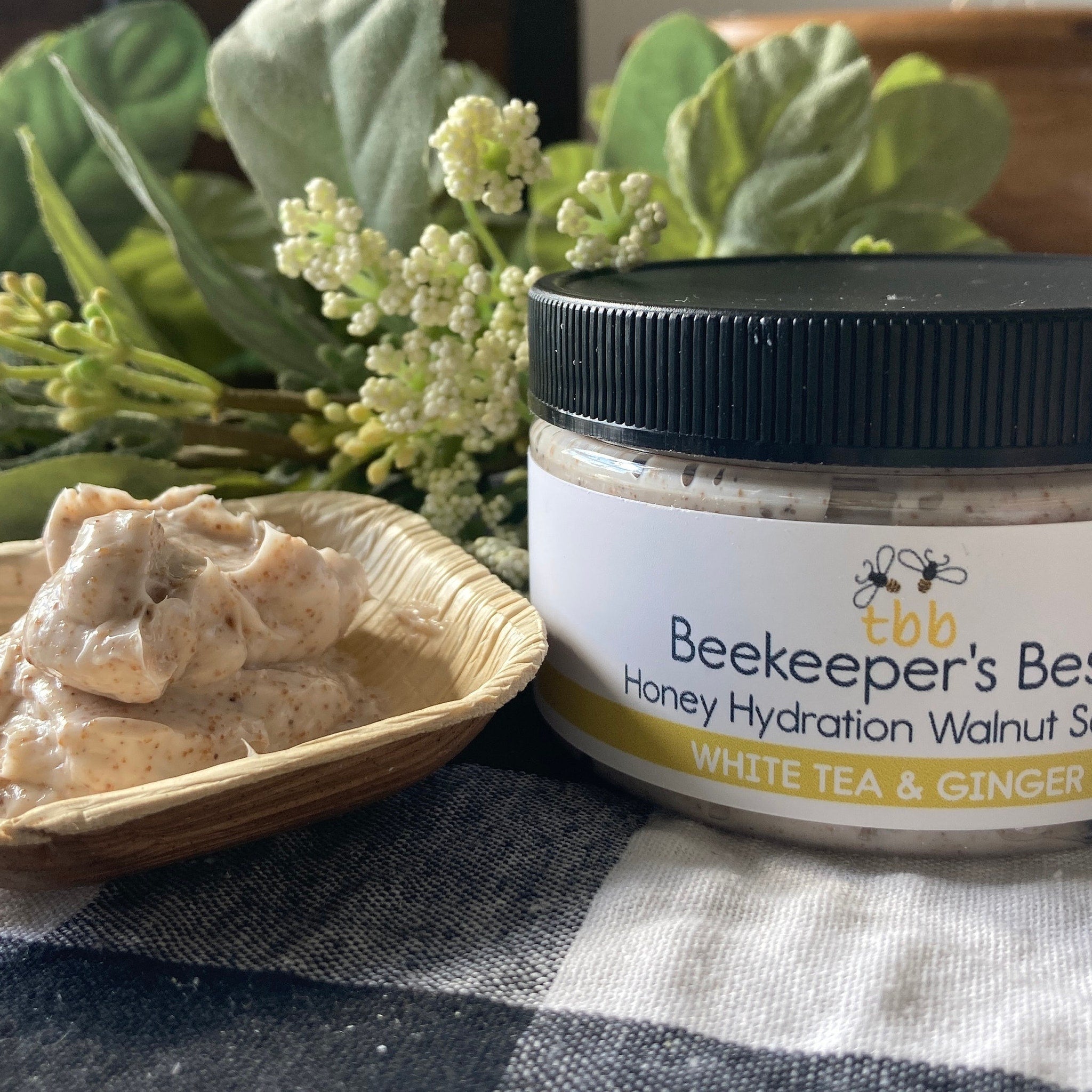 Honey hydration walnut scrub in jar with black lid, tbb logo, and white label on checkered cloth