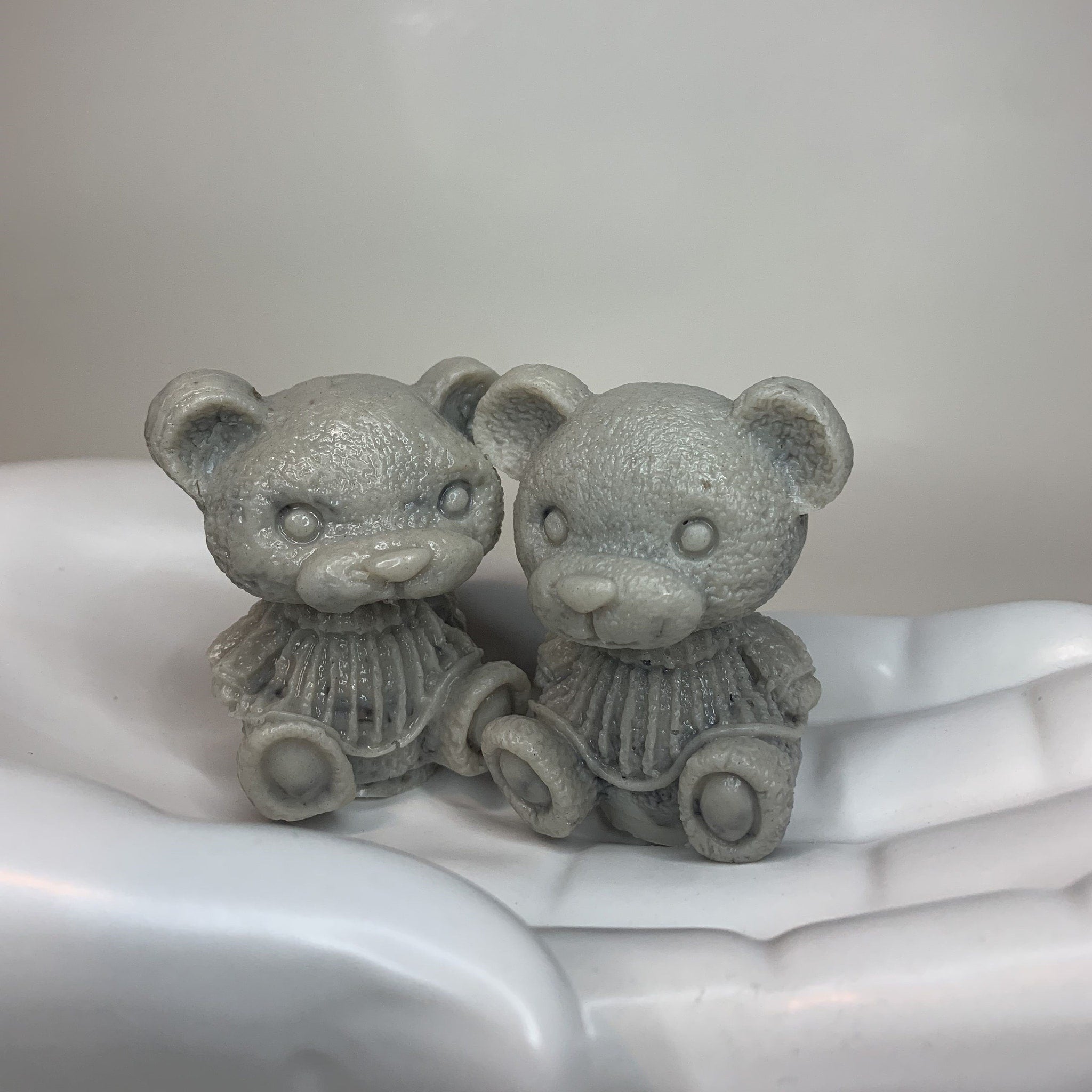 Grey teddy bear figurines with textured surface and ruffled collar, sitting in a white hand-shaped dish