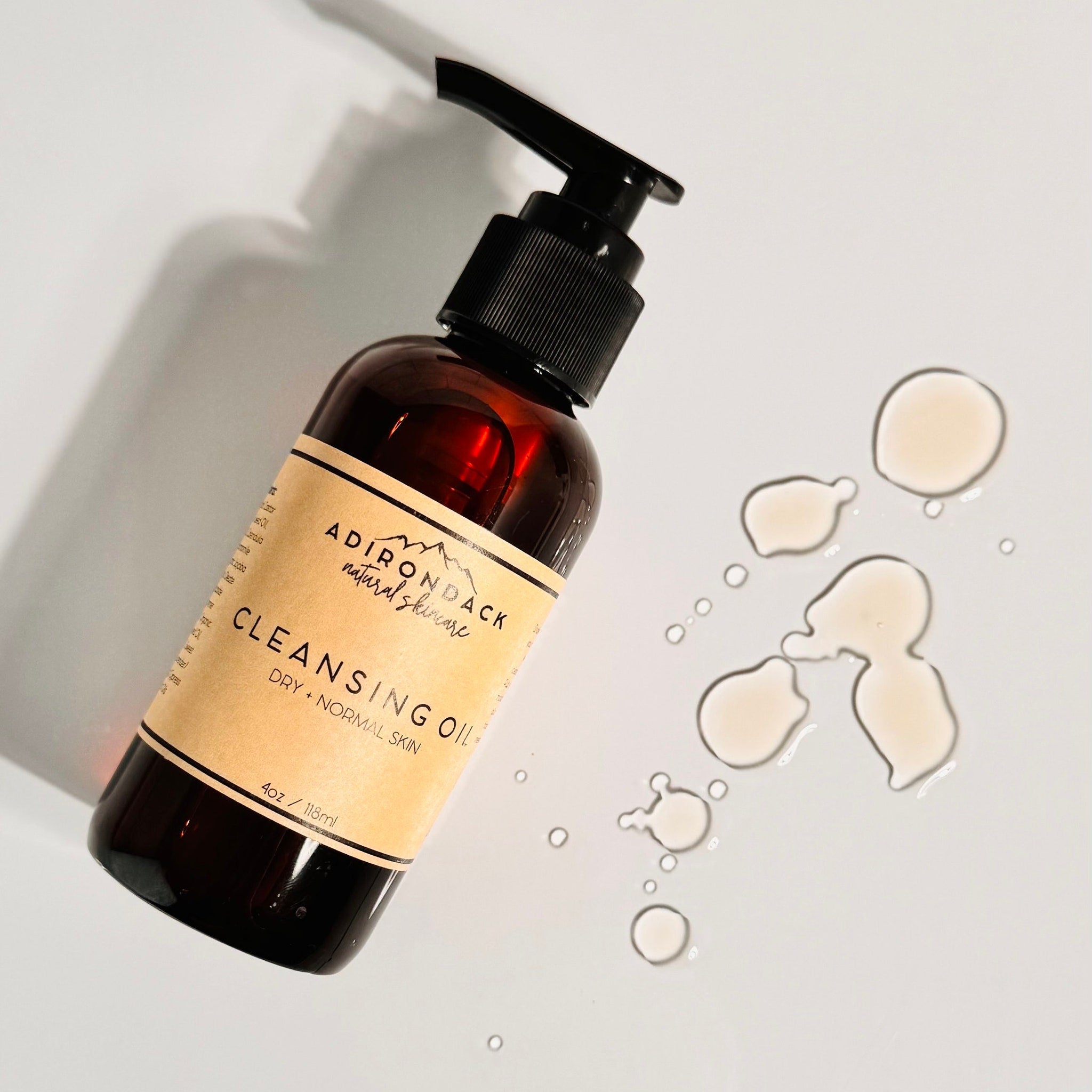 Cleansing oil bottle with brown glass, black pump, and tan label, with spilled oil drops