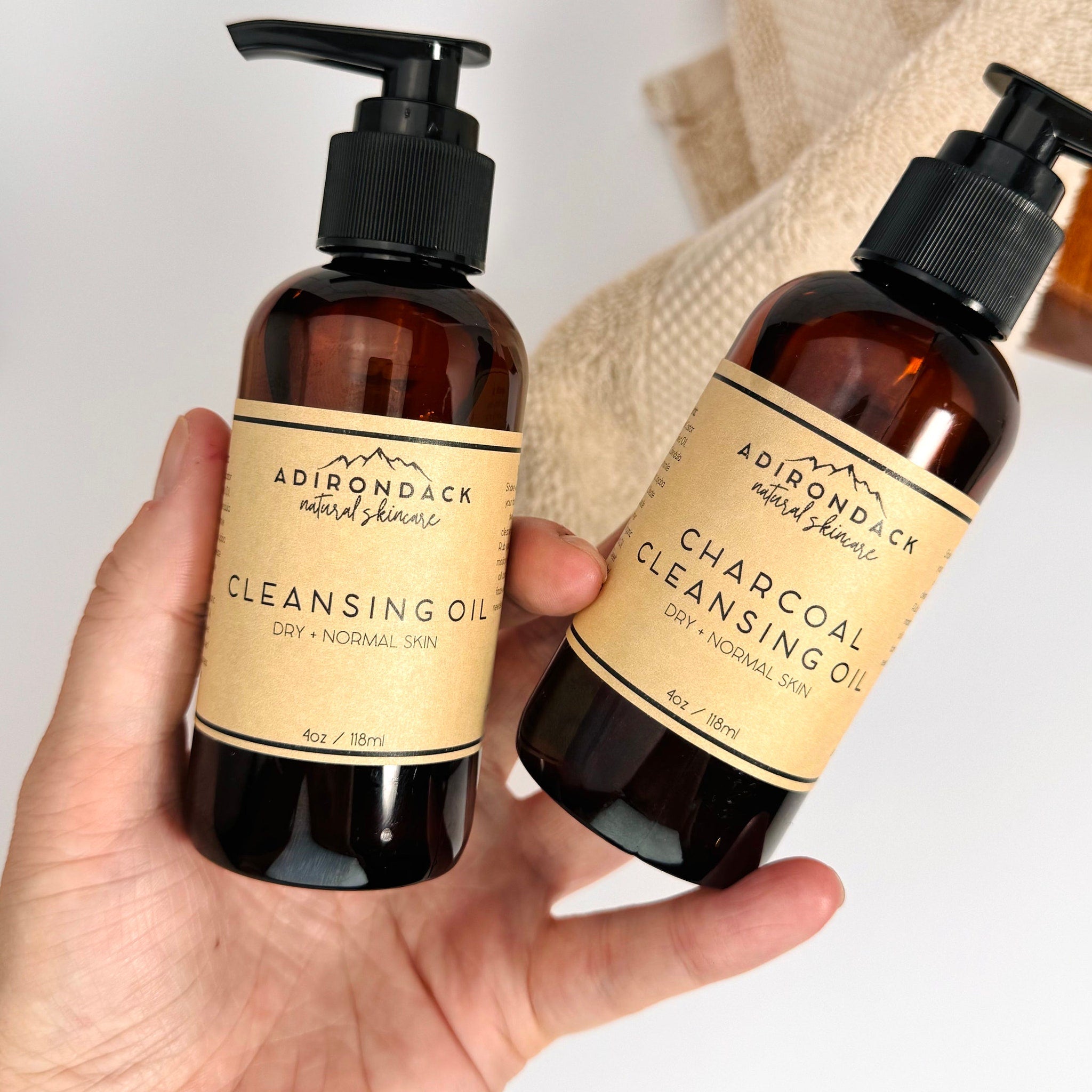 Cleansing oil bottles with brown glass, black pump tops, and tan labels, held by hand, Adirondack brand visible