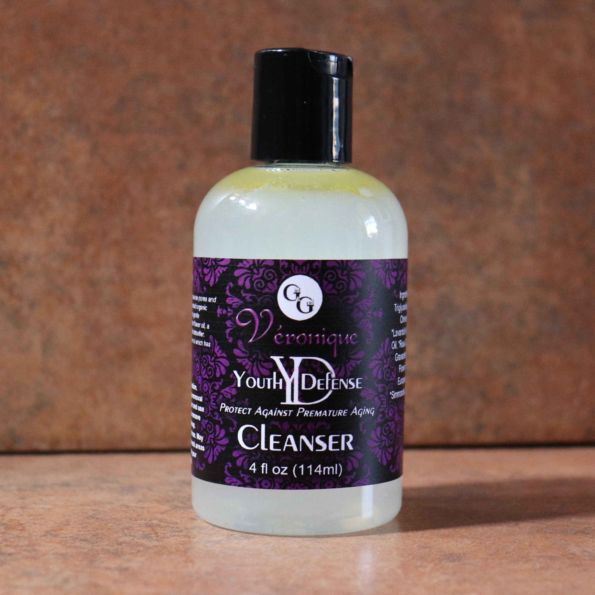 Cleanser bottle with black cap, white label, and purple floral pattern, Véronique Youth Defense brand