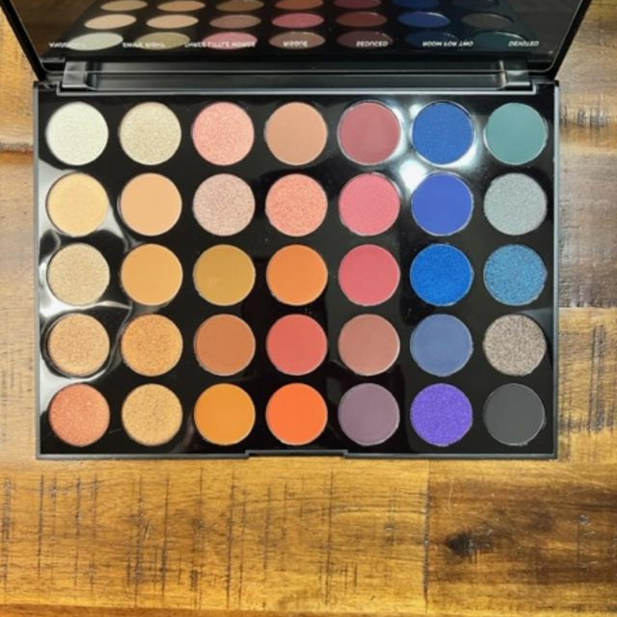Eyeshadow palette with various colors, including orange, blue, and purple, in a black compact case