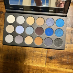 Eyeshadow palette with various colors including blue, silver, and brown in a black case