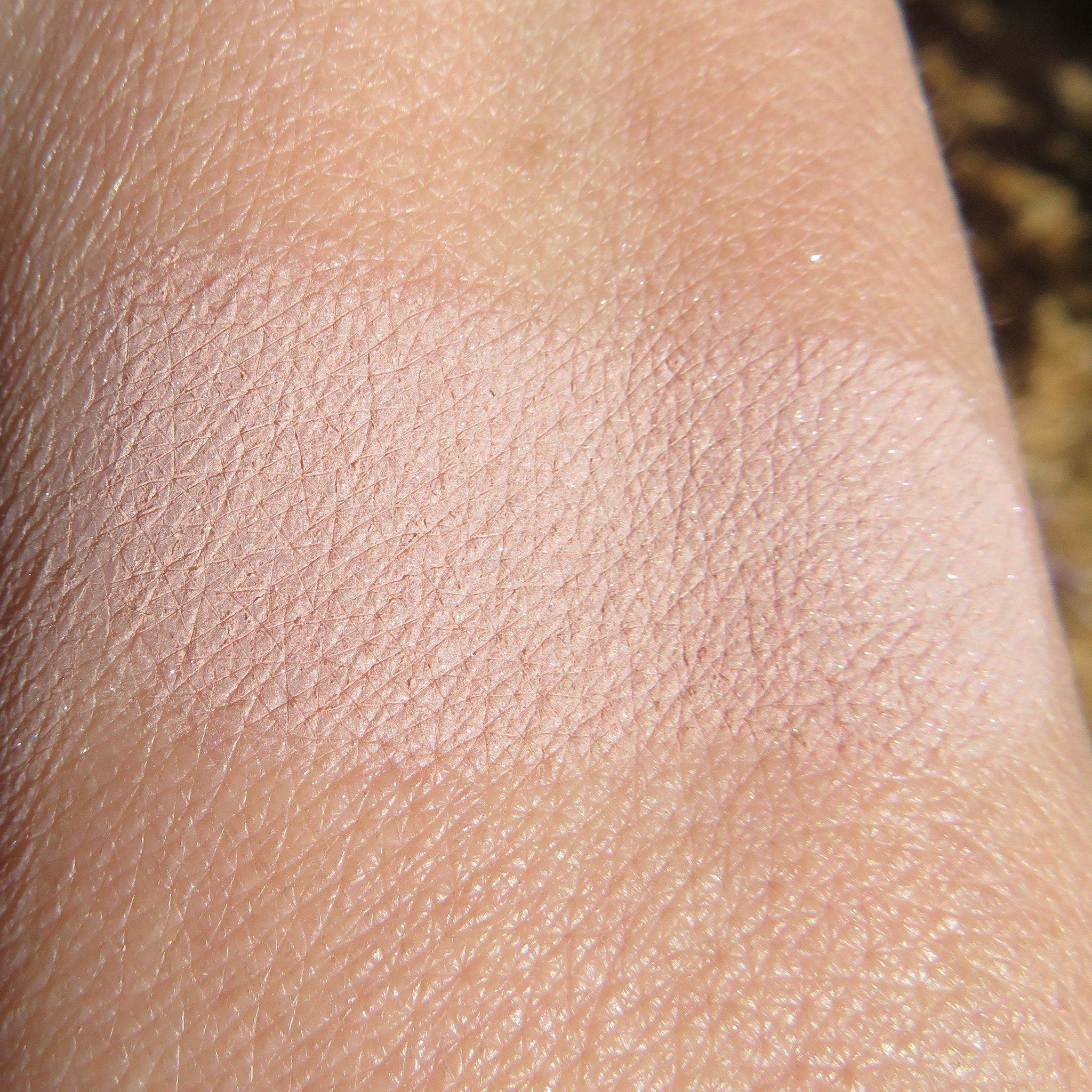 Side view of loose sandy brown shimmer eyeshadow pigment spilling from jar, showcasing fine metallic particles.