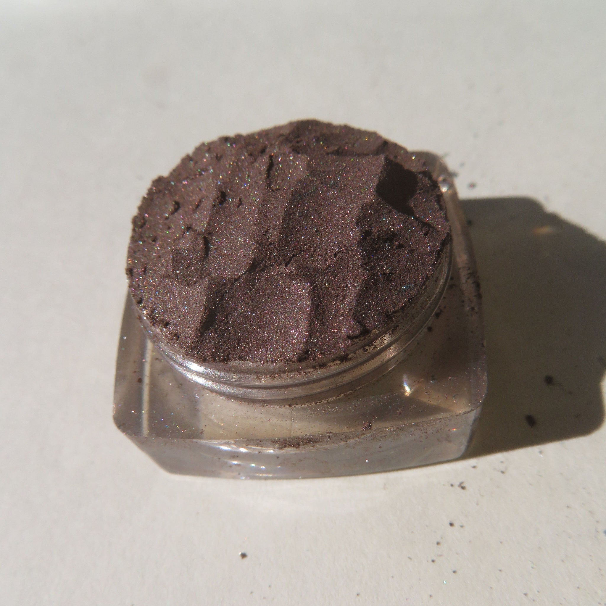 Close-up of rich dark brown vegan loose mineral eyeshadow with shimmer pigment, cruelty-free, in a small jar.