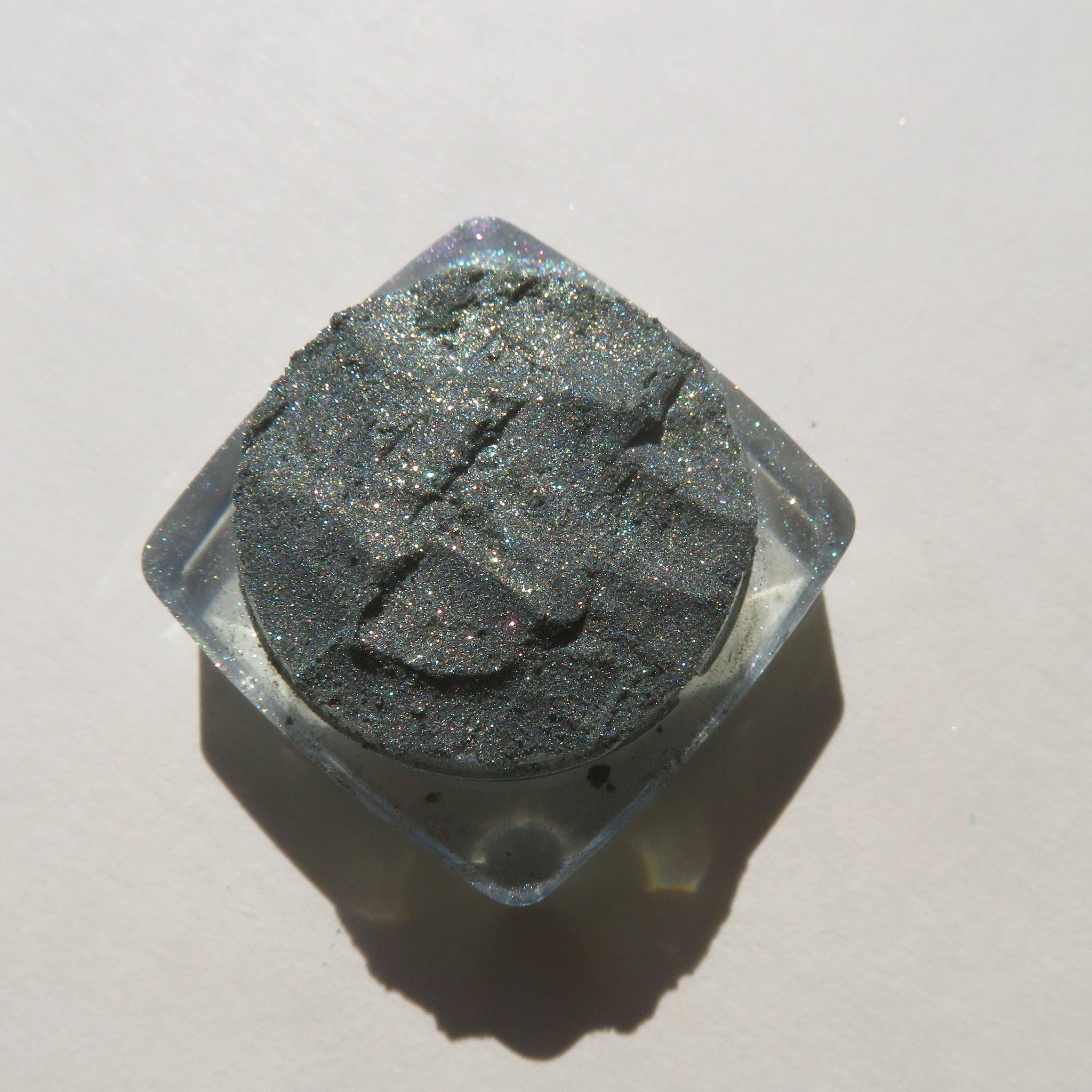 Glitter eyeshadow in dark gray with clear container, top-down view