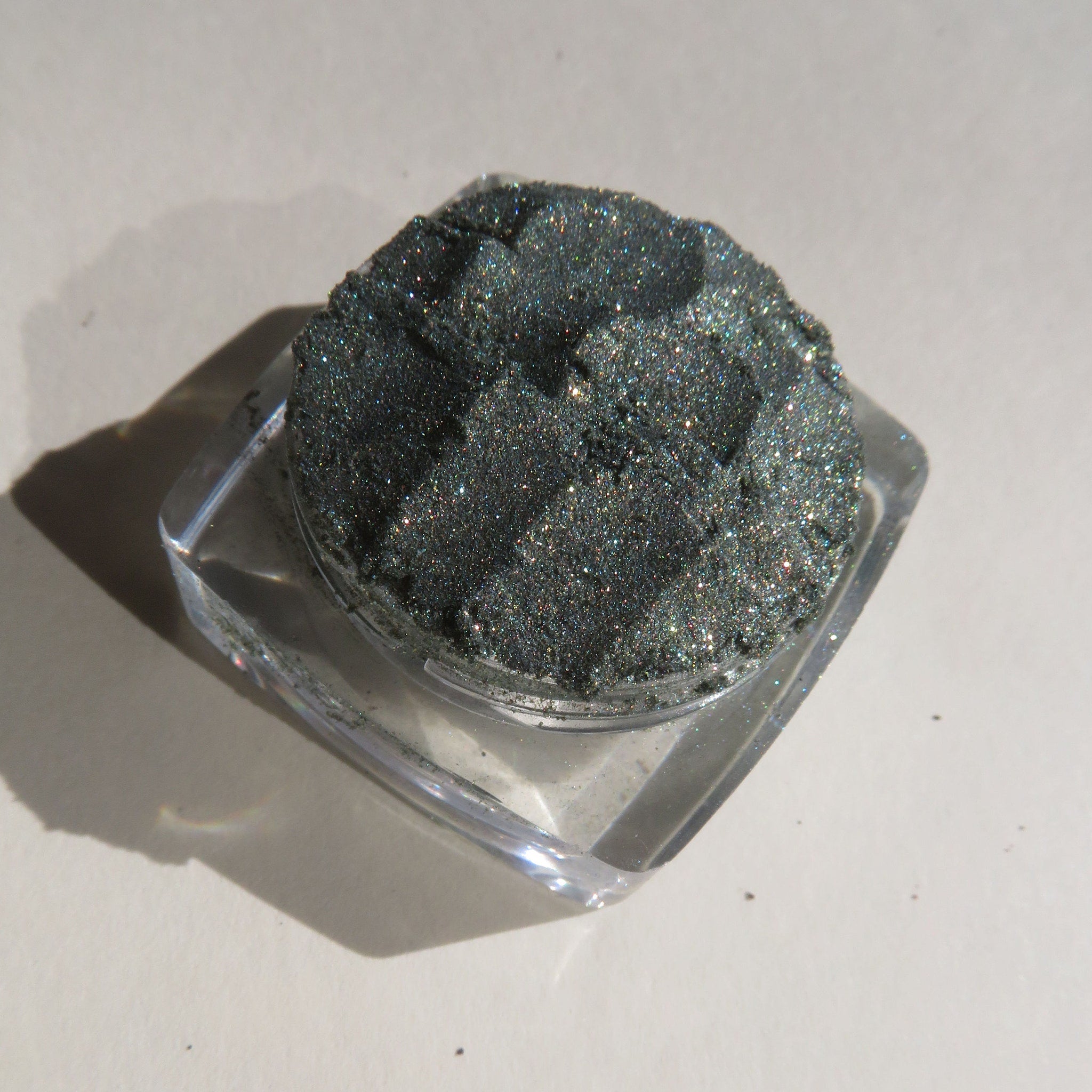 Glitter eyeshadow in dark green with sparkly finish, in clear square container