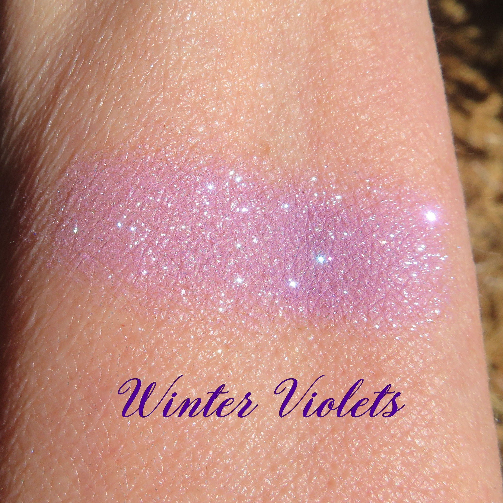 Close-up of Winter Violets eye shadow pan showing intense purple-blue glitter particles catching light