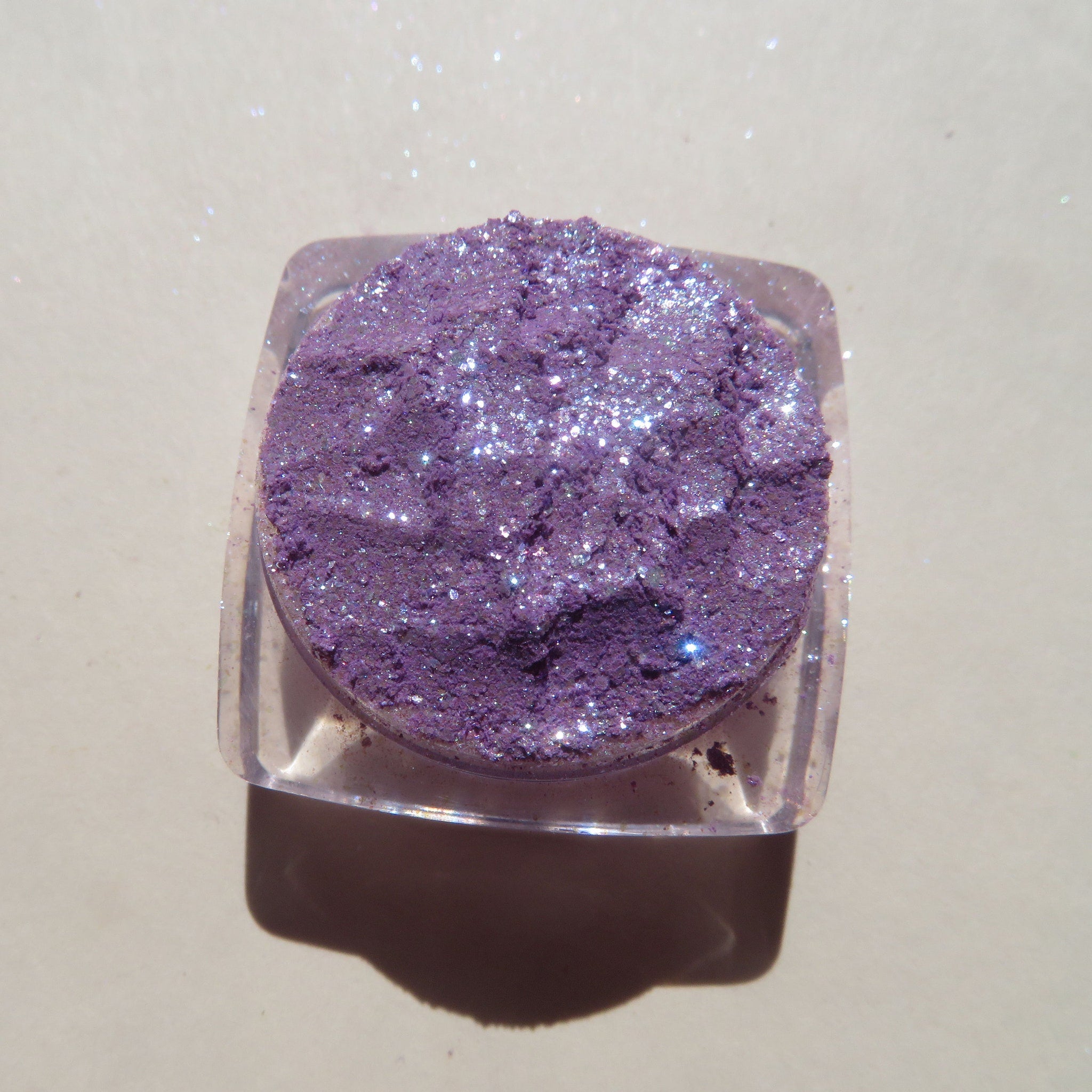 Open compact showing Winter Violets shimmer eye shadow with purple and blue glitter swirls on white background