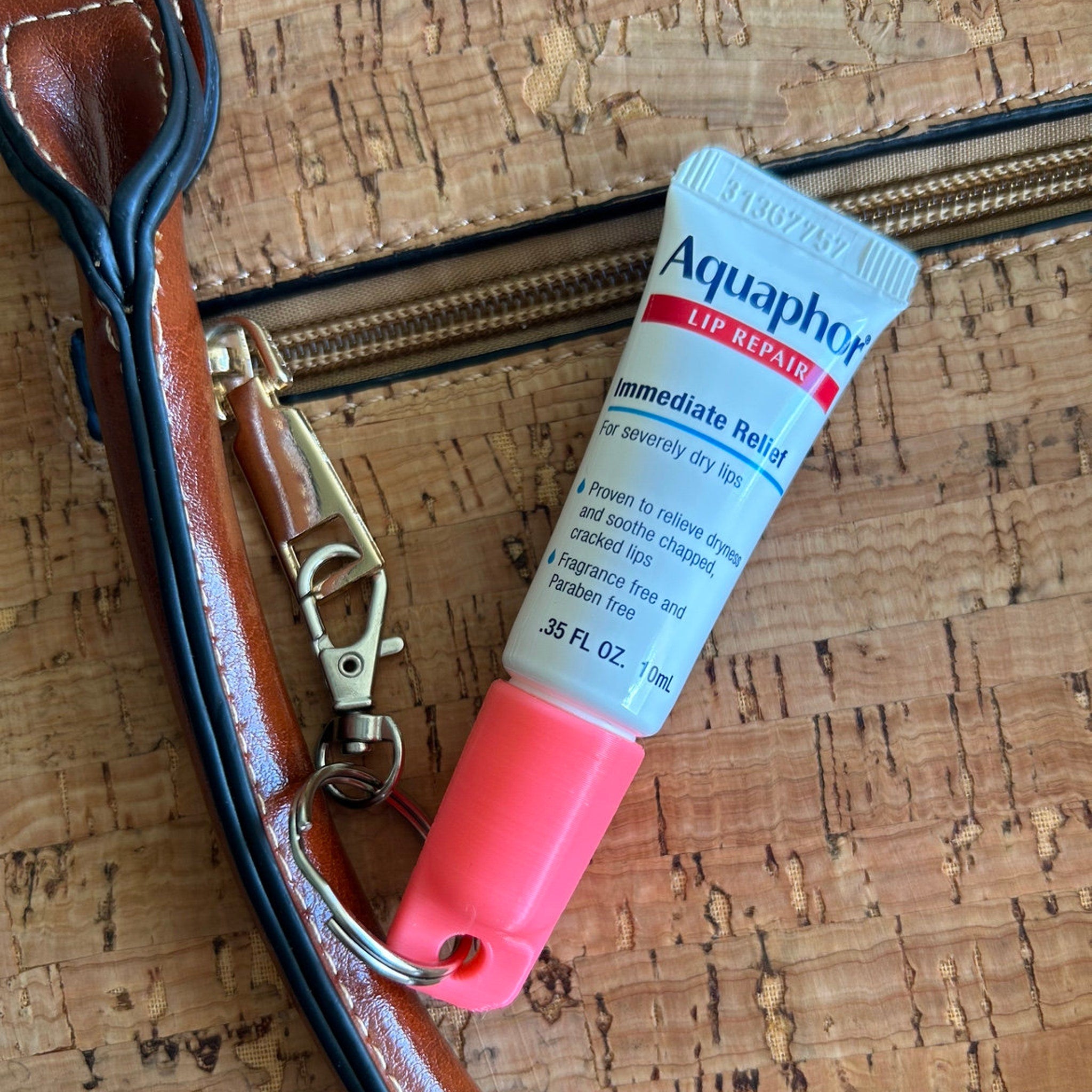Aquaphor lip repair tube with pink cap, white and blue label, and brown cork background