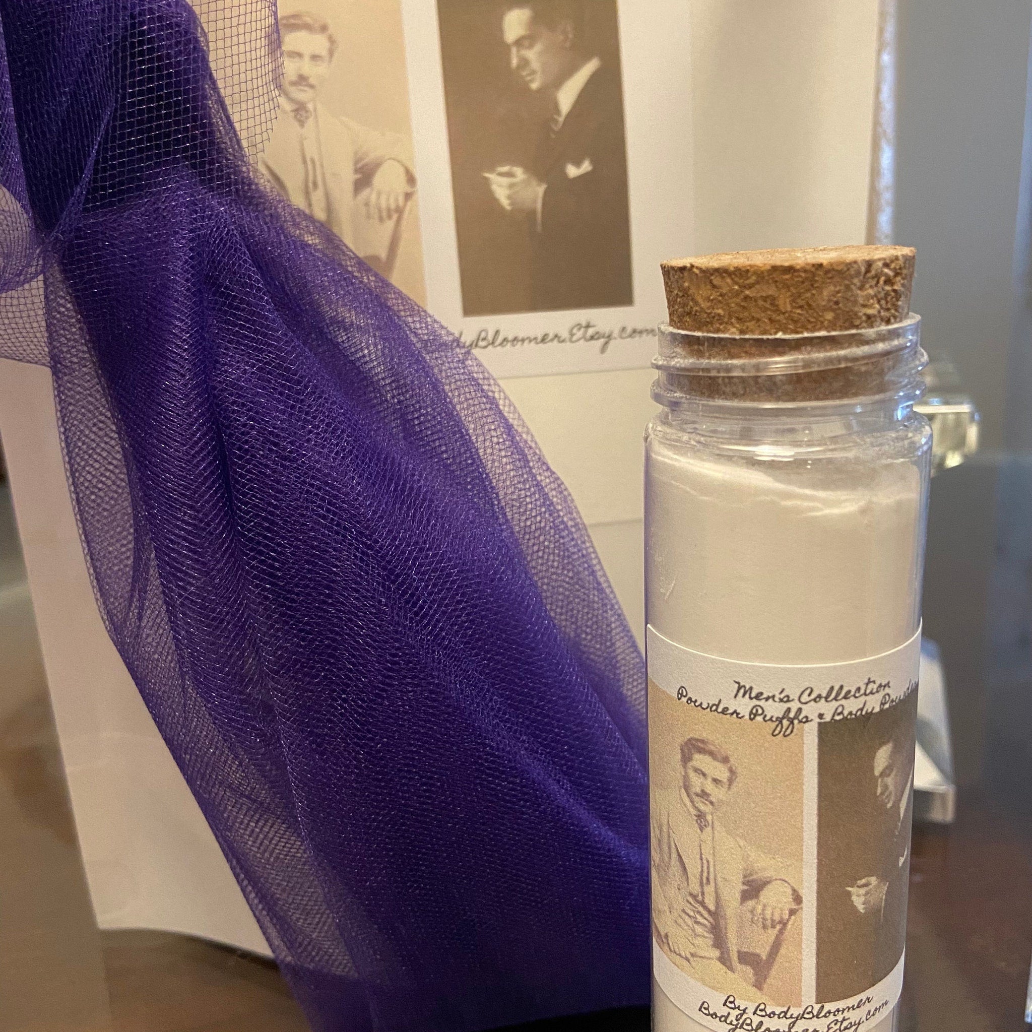 Body powder bottle with cork stopper, Men's Collection label, and purple mesh fabric background