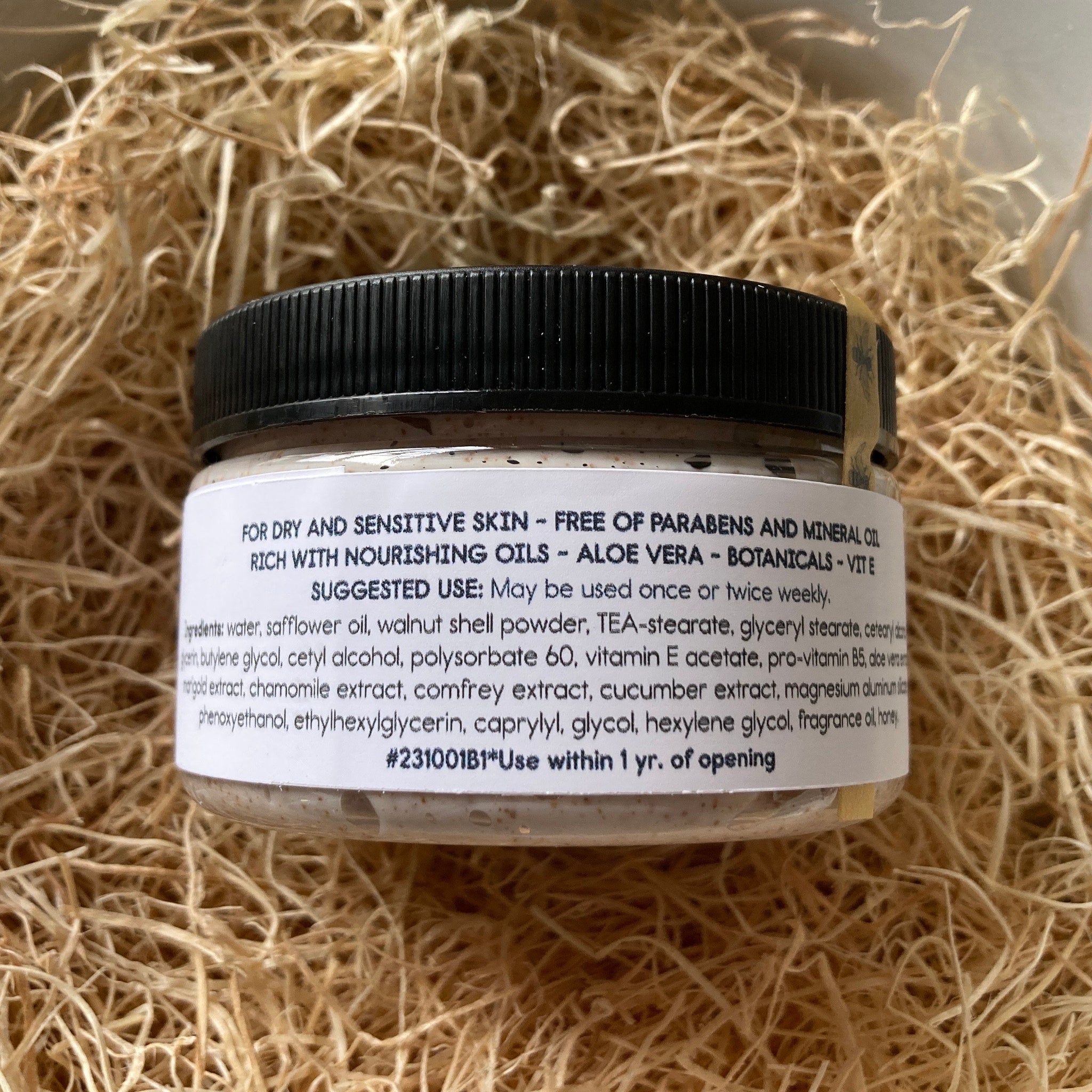 Jar of cream with black lid, beige contents, and white label on straw background