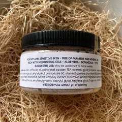 Jar of cream with black lid, beige contents, and white label on straw background