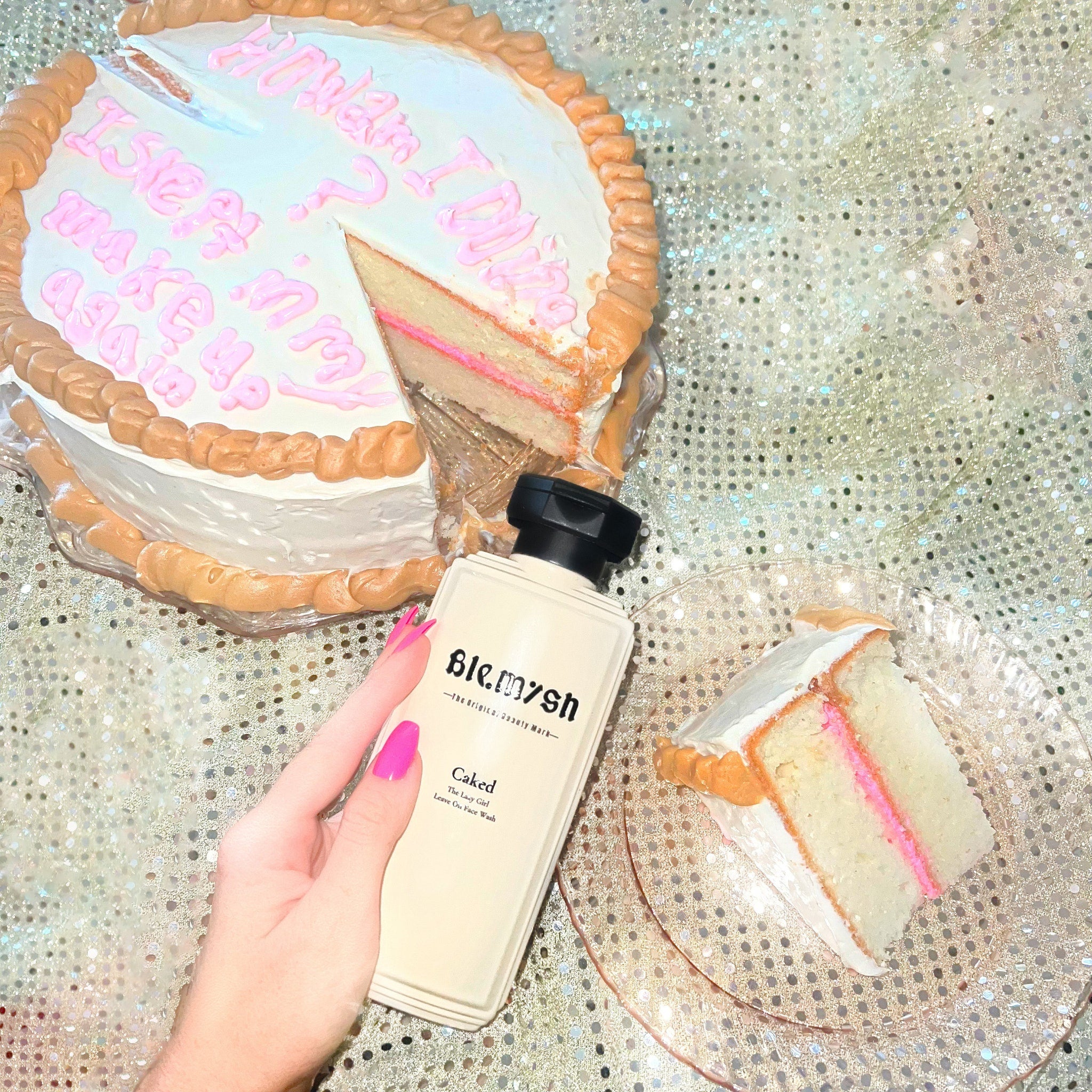 Cake with white frosting, pink filling, and brown border, with "Ble.mysh" bottle and hand with pink nails