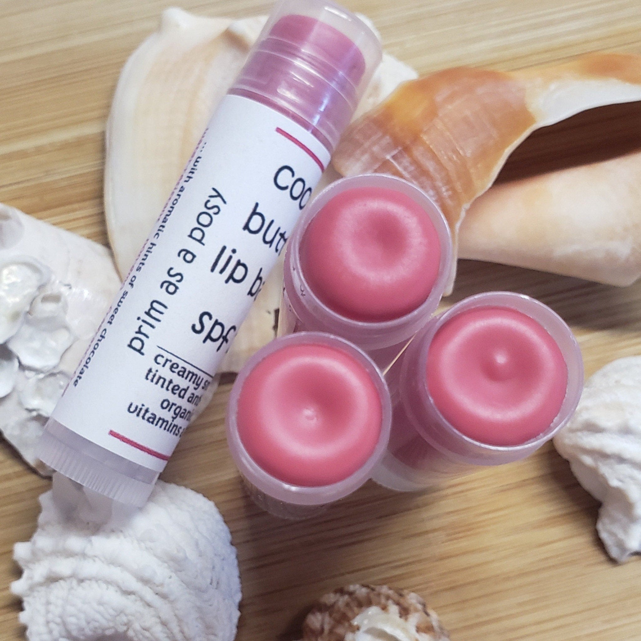 Lip balm tubes with pink color, clear plastic, and Twin Oaks Naturals branding on a wooden surface