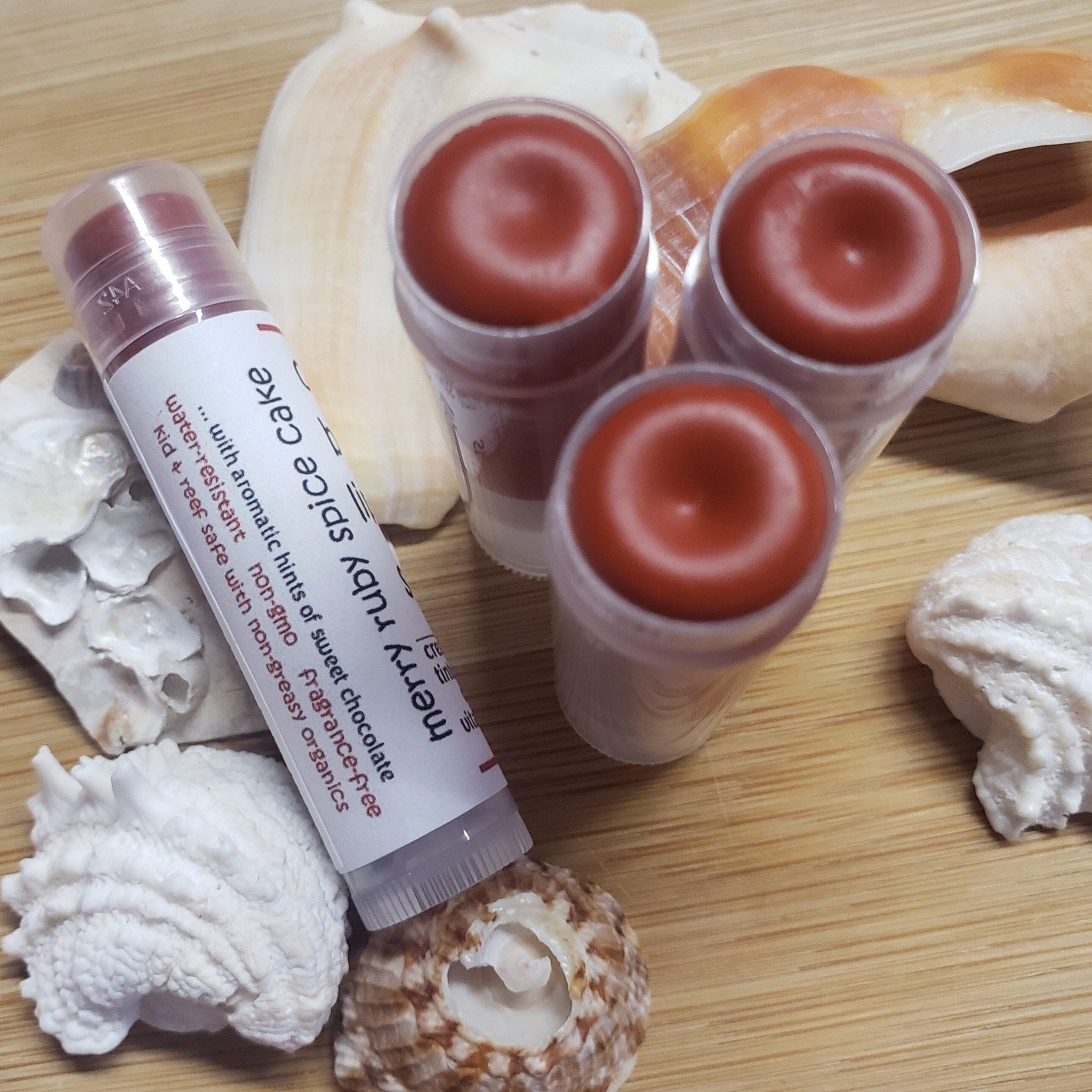 Lip balm tubes with red balm, clear plastic, and white label on wooden surface