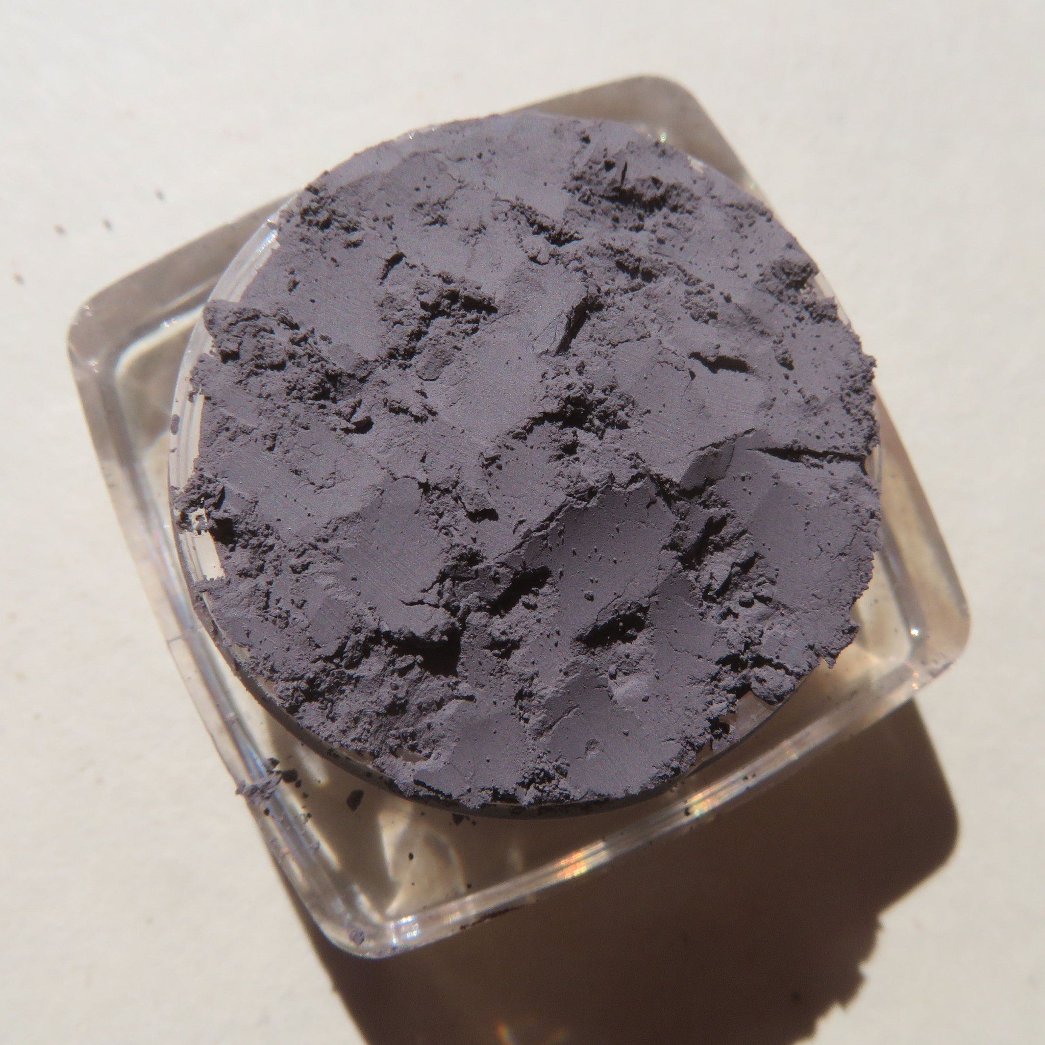 Open jar of matte medium gray mica mineral eyeshadow with loose powder visible inside