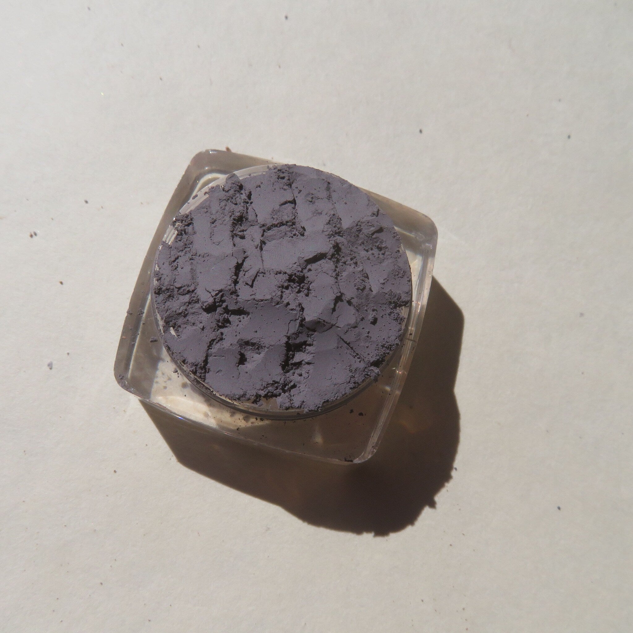 Side view of matte medium gray mica mineral eyeshadow in loose powder form, showcasing subtle shimmer texture