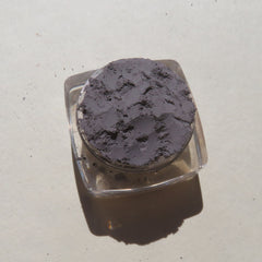 Powdered eyeshadow in gray, textured surface, contained in clear plastic jar