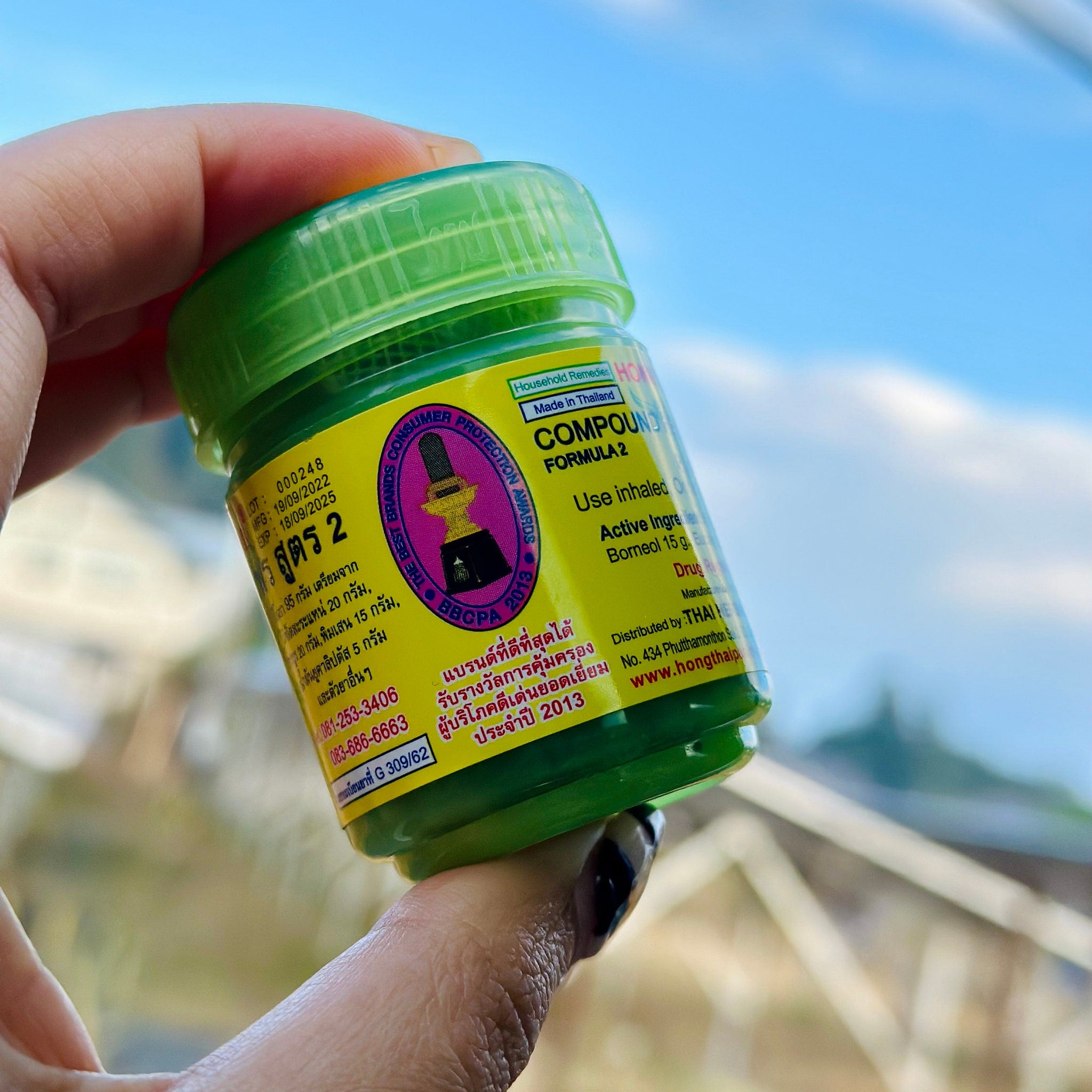 Green jar with yellow label, green lid, held in hand against blue sky