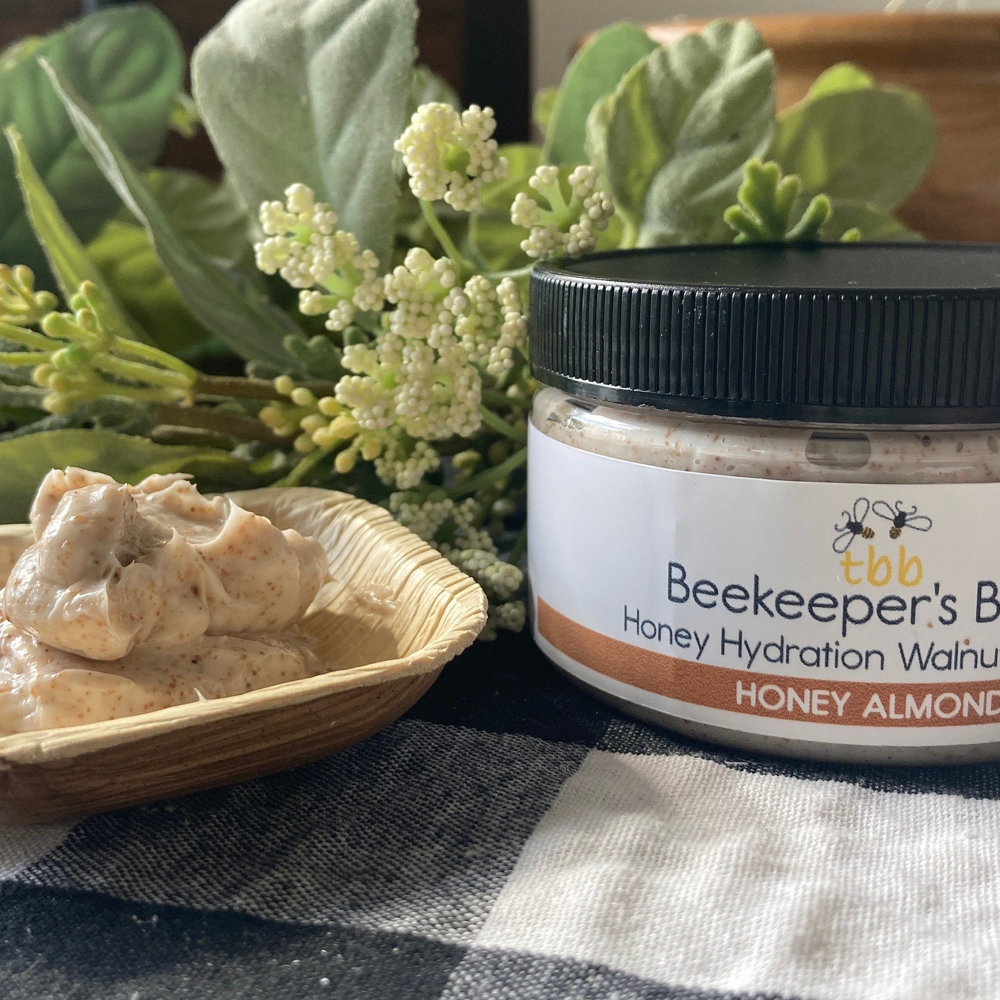 Honey hydration walnut scrub with black cap, white label, and wood bowl on checkered cloth